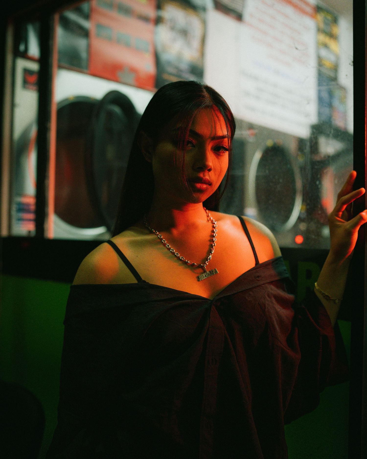 Moody atmospheric portrait of a person wearing a dark top and chain necklace sitting in a dimly lit transit vehicle.