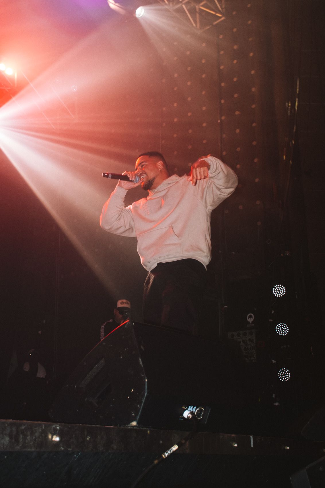 Concert performer in white sweater singing passionately under dramatic red stage lighting.