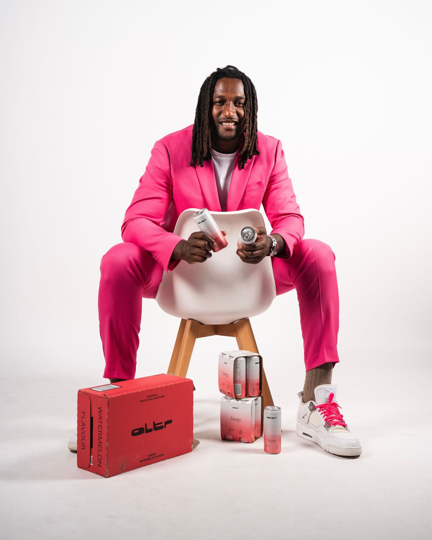 Person in bright pink suit sits on white chair with energy drinks and accessories.