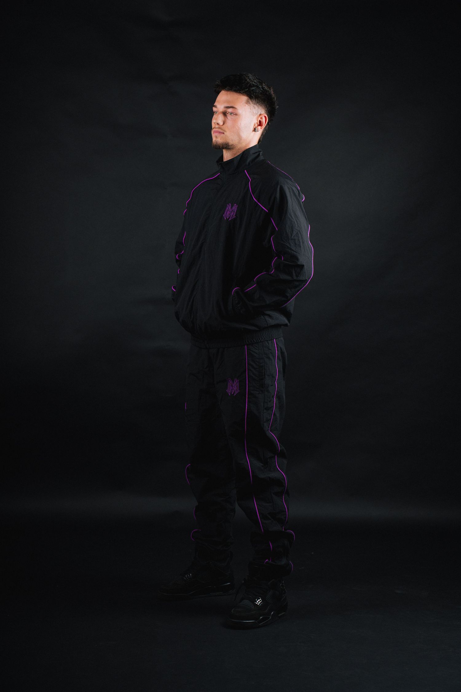 Full body shot of person in black tracksuit with purple accents against dark background.