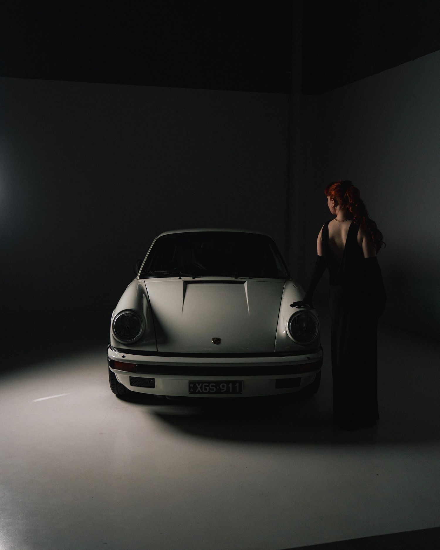 Classic white Porsche 911 photographed in dark studio with silhouette beside it.