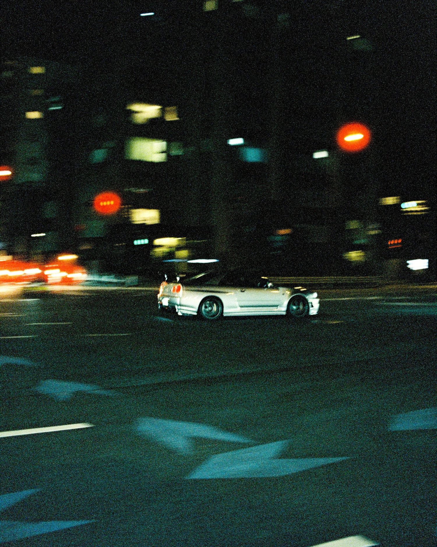 White sports car driving through city streets at night with blurred lights in background.