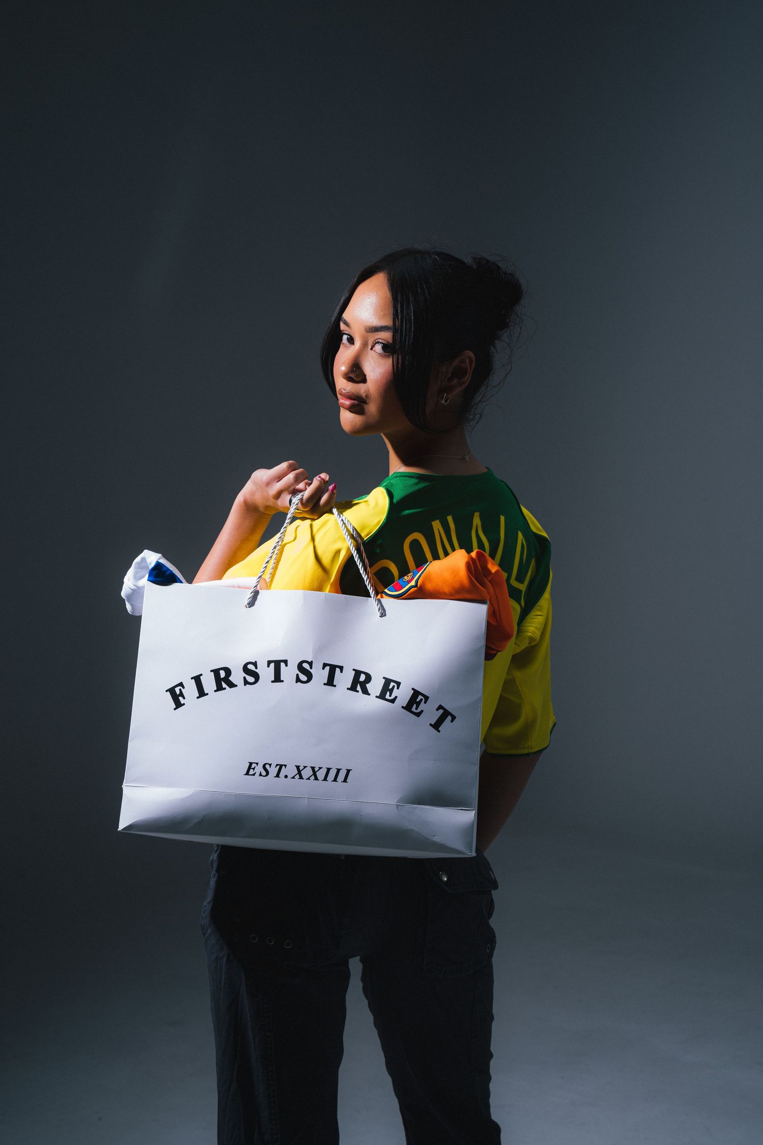 Fashion model posing with FirstStreet shopping bag against dark background.