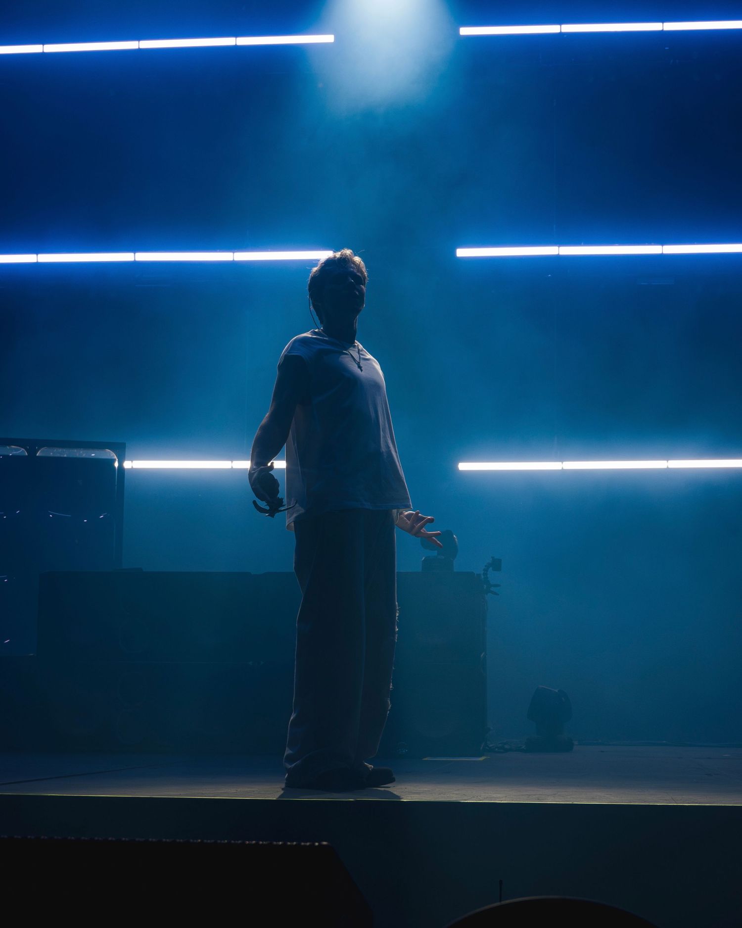 A silhouetted performer stands on stage with dramatic blue lighting and horizontal light beams creating an atmospheric scene.