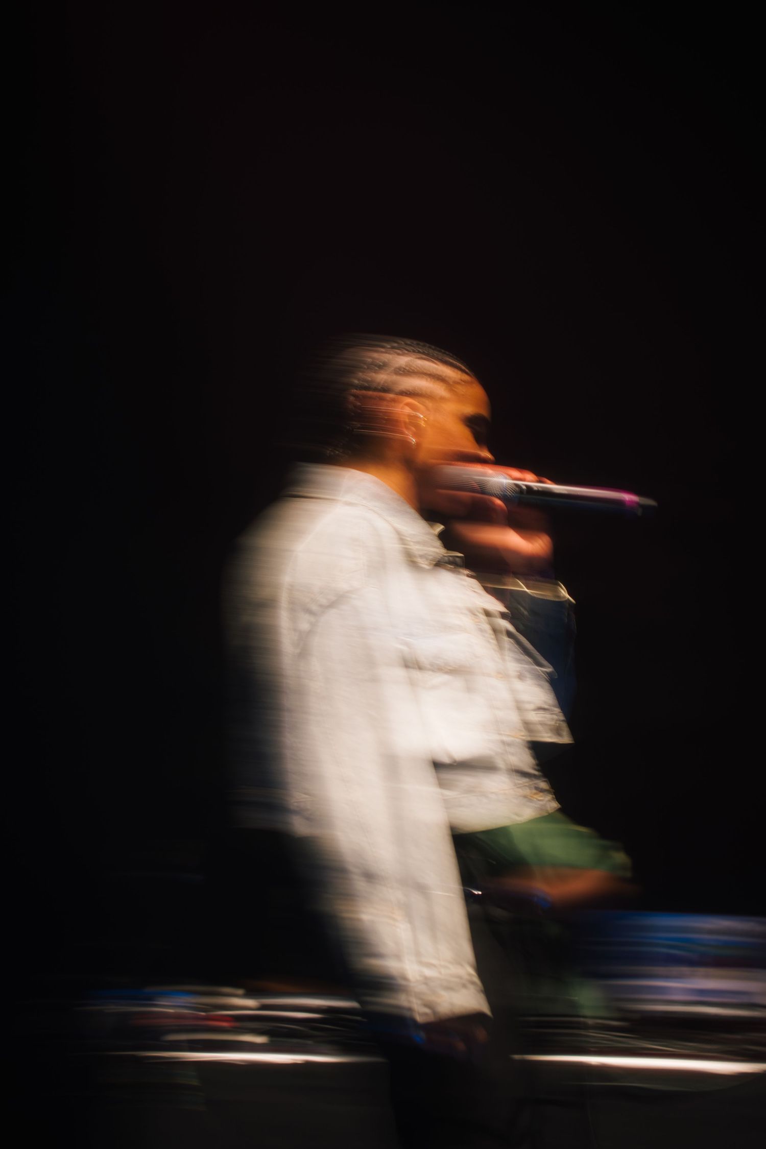 Blurred motion photograph of a performer in white clothing on a dark stage with microphone.