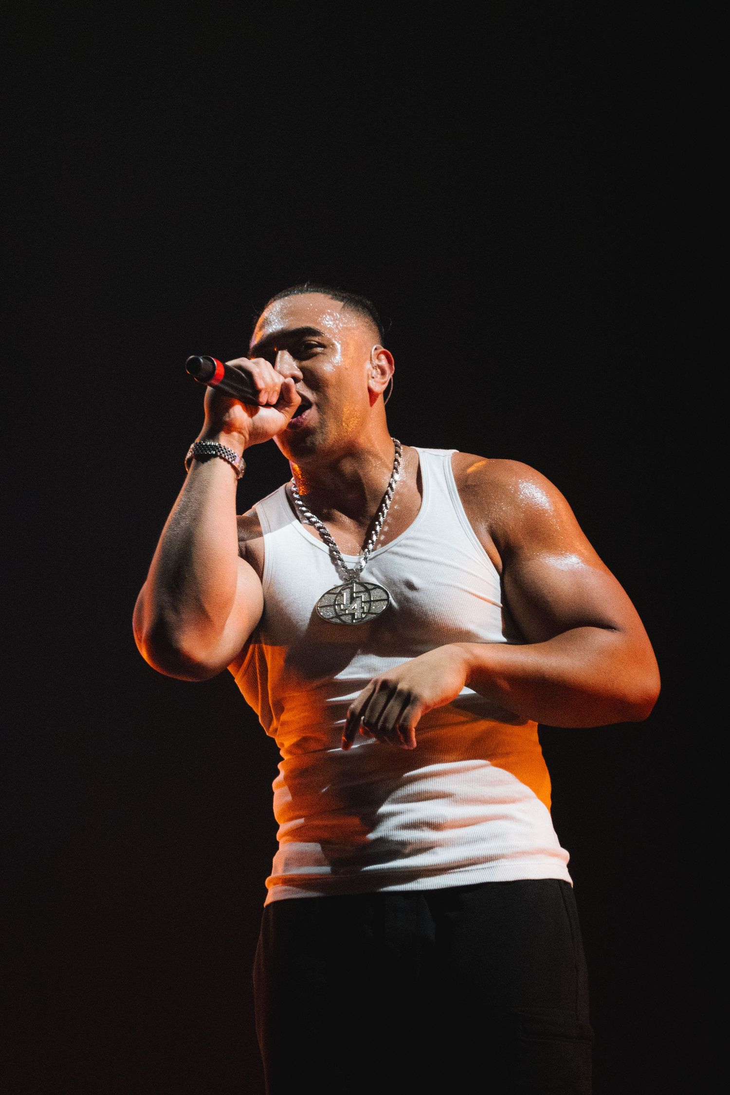 Energetic performer in white tank top singing passionately on stage with dramatic lighting.