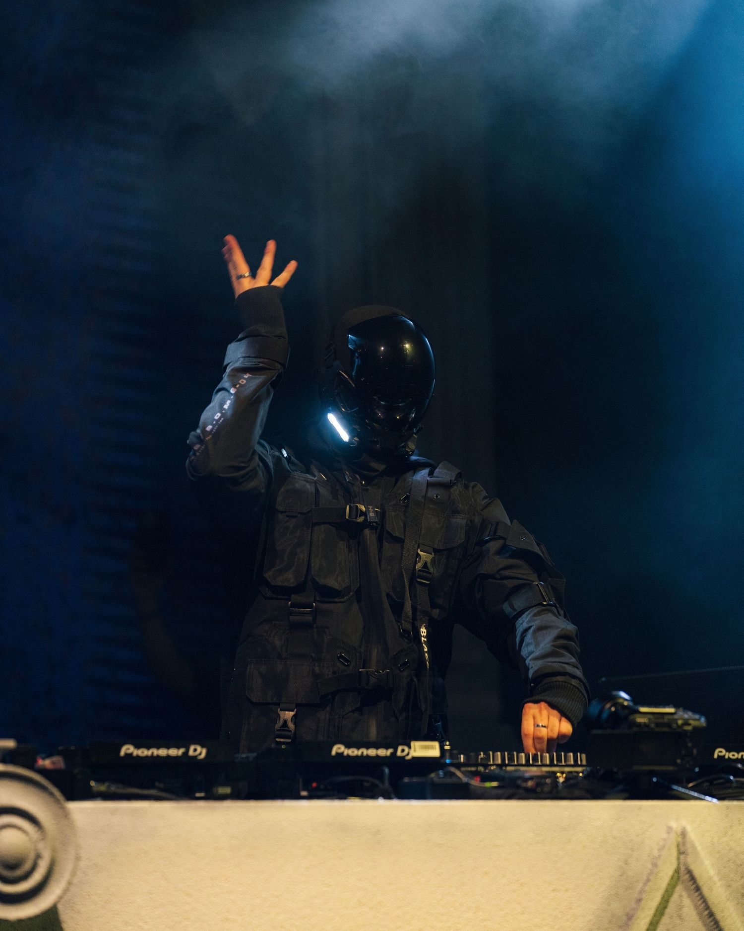 DJ in tactical gear and helmet performs at electronic music show with dramatic lighting.