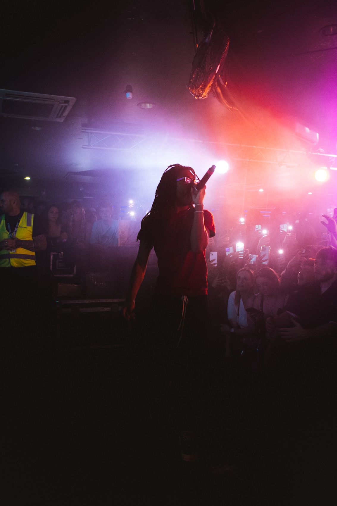 Silhouetted performer on stage with dramatic red and purple lighting creates atmospheric concert ambiance.