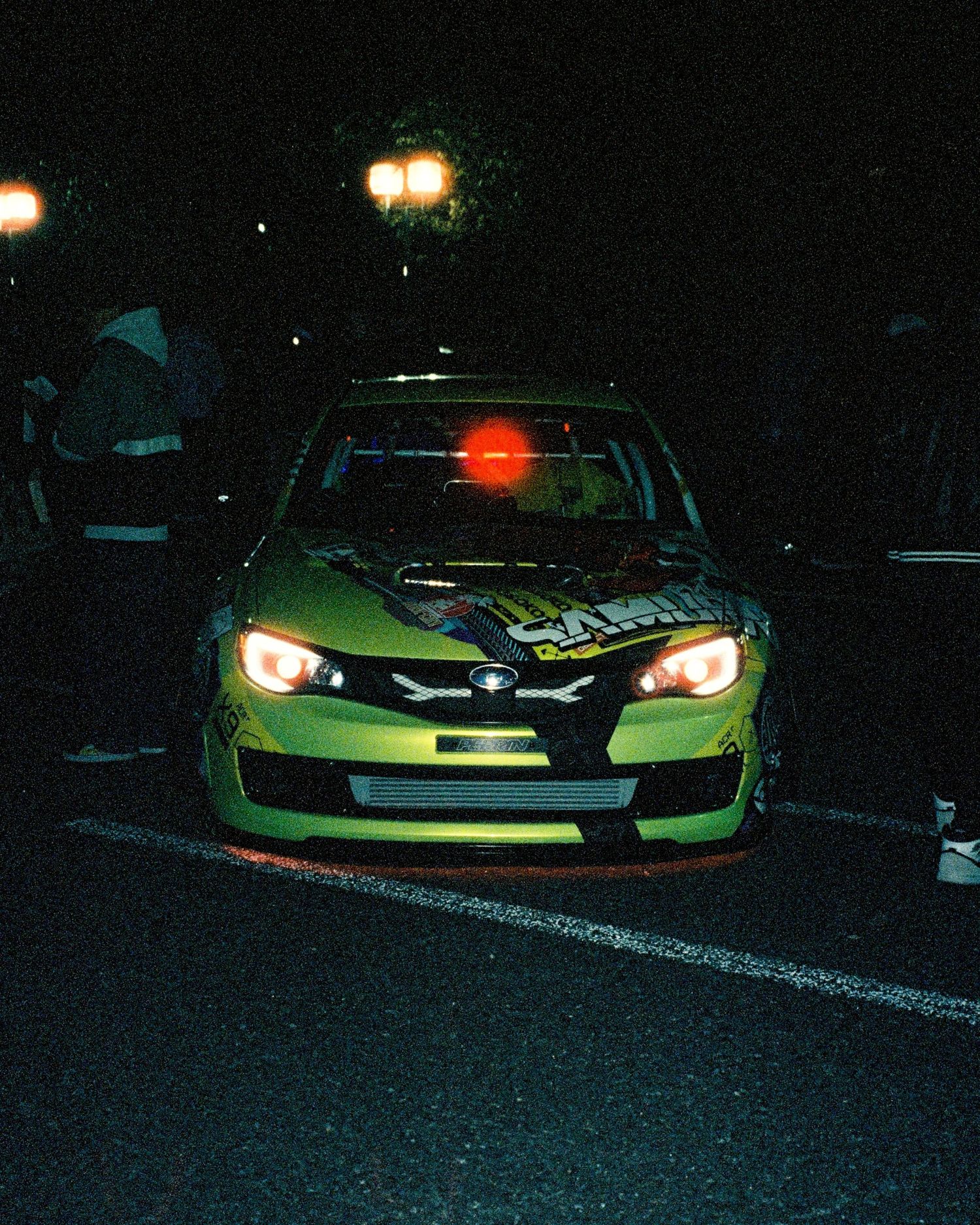 Lime green modified Subaru WRX with custom headlights captured at night meet.