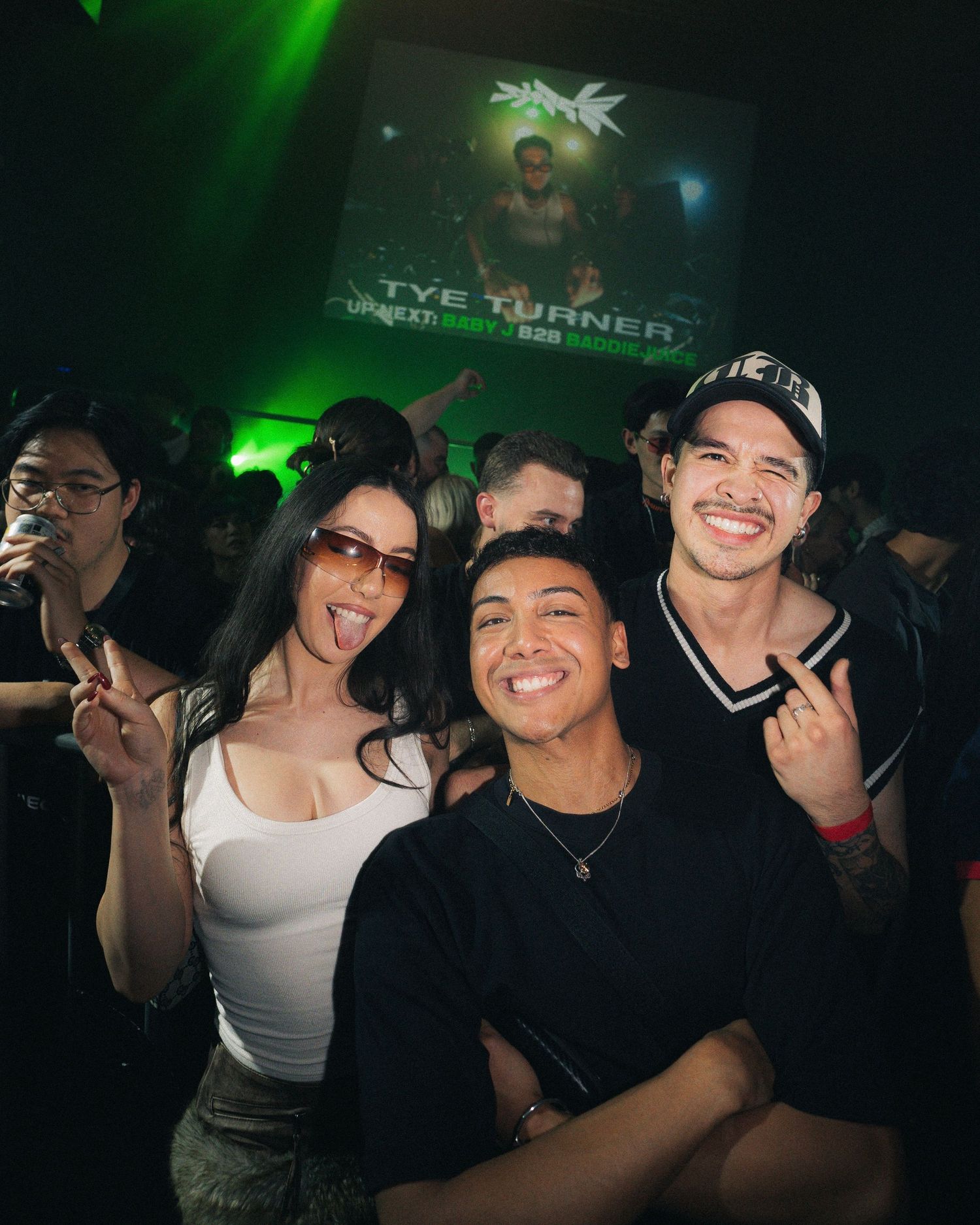 Group of friends posing for photo at club with green lighting and screen in background.