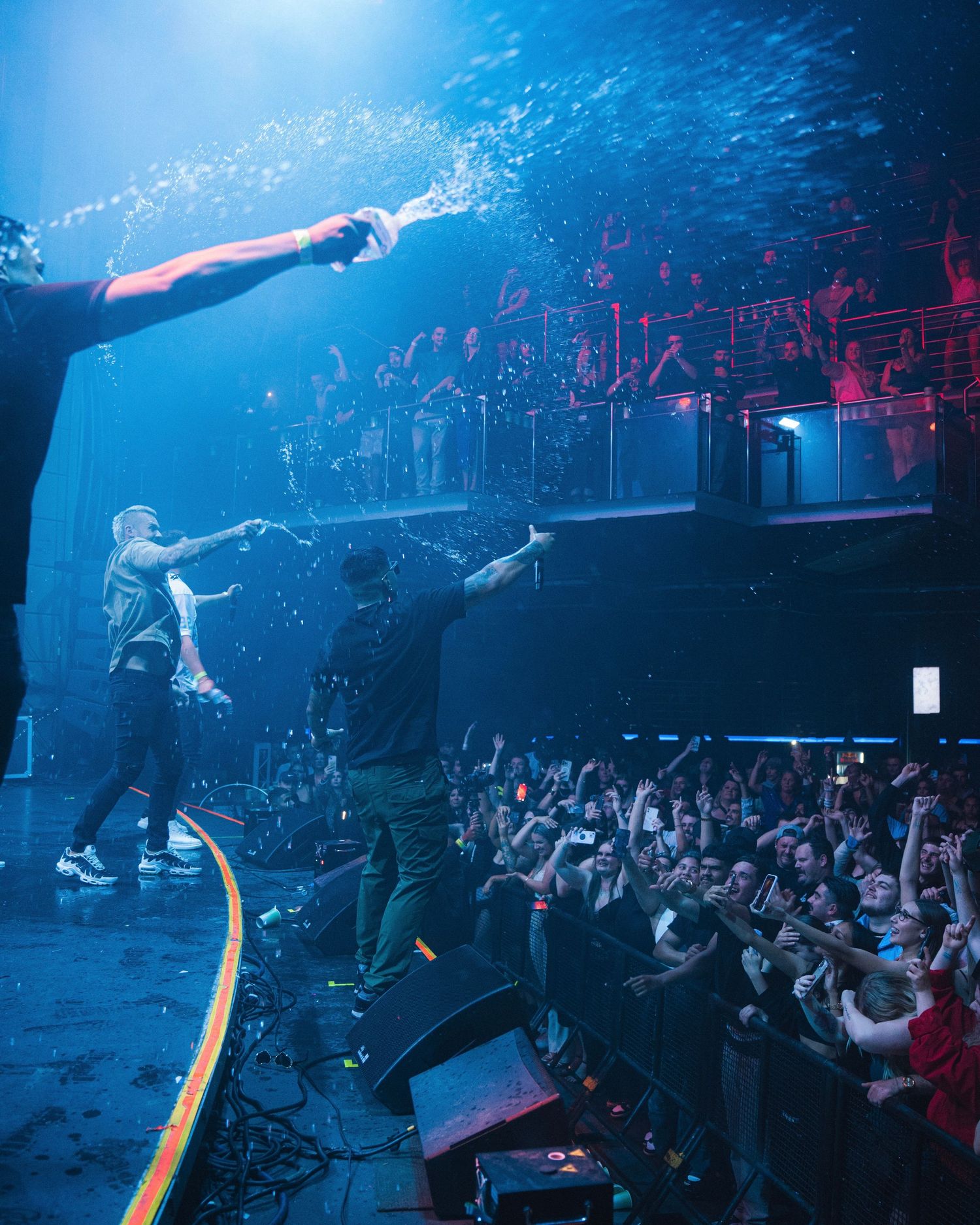 Concert performers on stage with dramatic blue lighting and crowd silhouettes below.