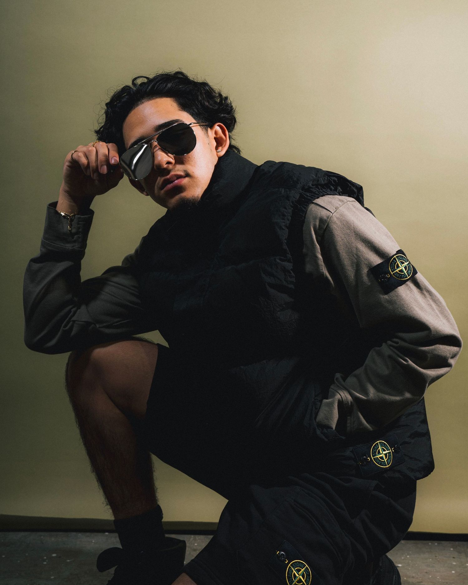 Stylish portrait featuring Stone Island sportswear and sunglasses against neutral background.