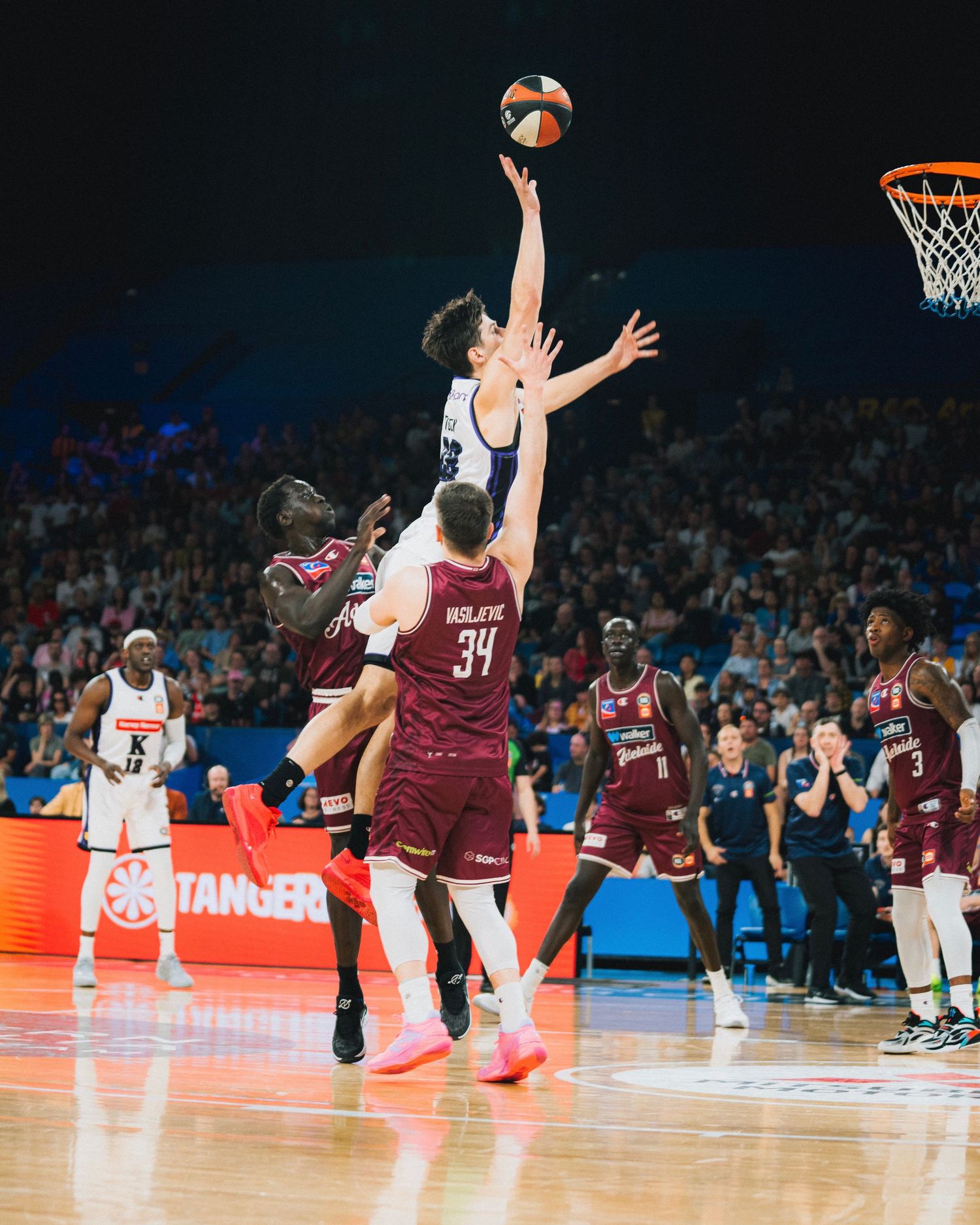 Basketball player leaping for layup during competitive game with defenders.