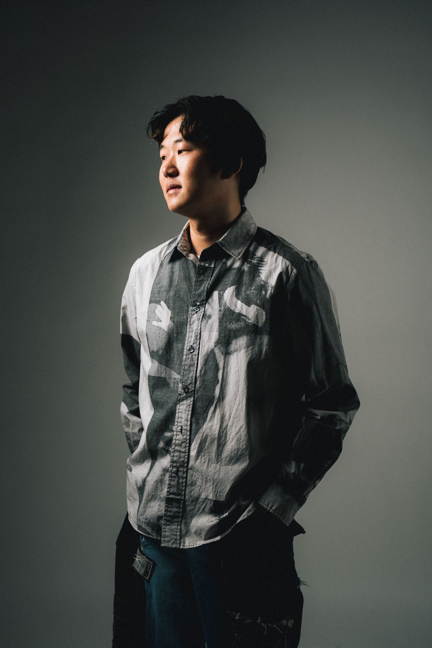 Dramatic studio portraits of someone in a gray button-down shirt with moody lighting against a dark background.