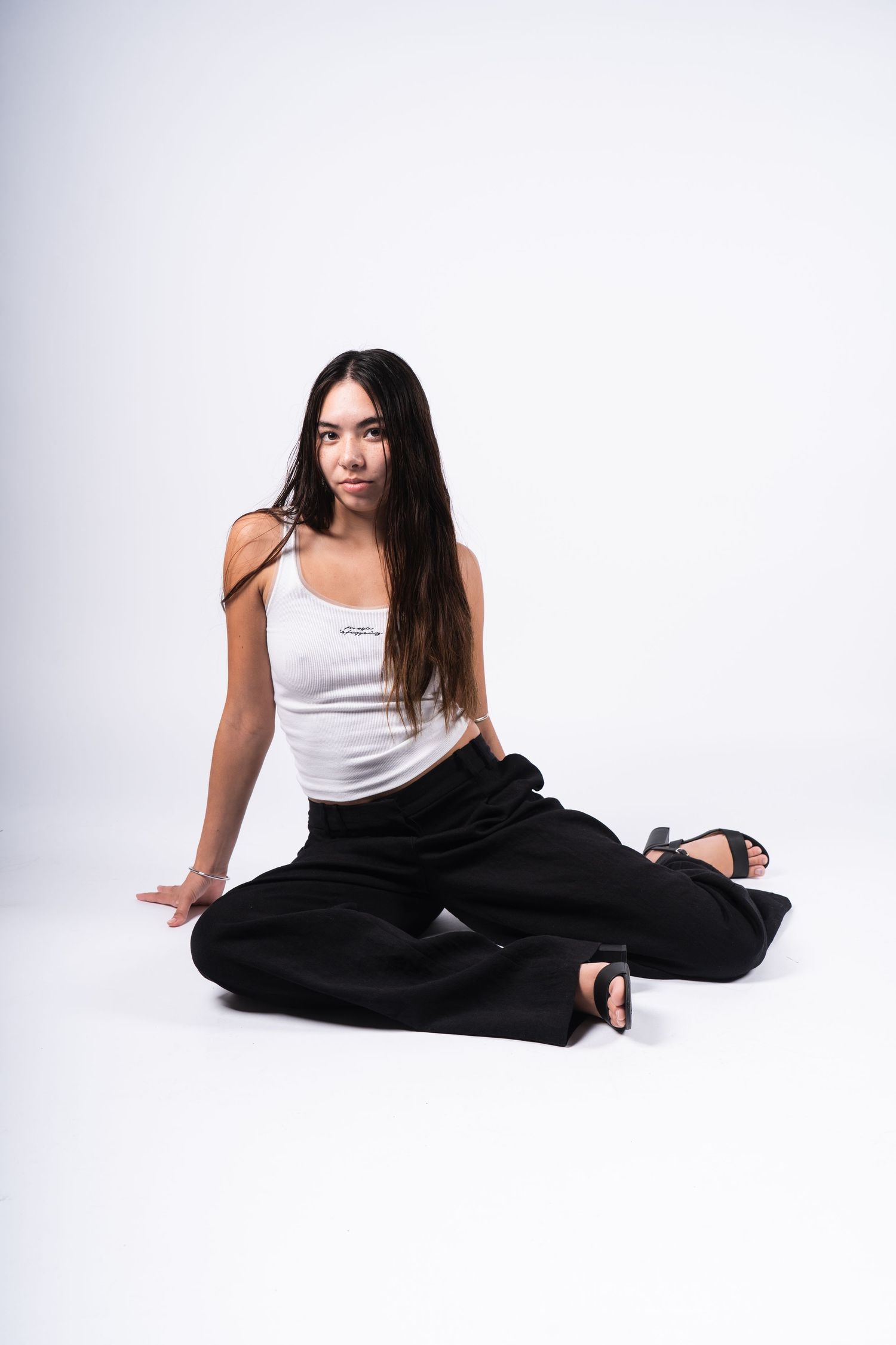 A person in a white tank top and black pants does a graceful yoga pose sequence on a light background.