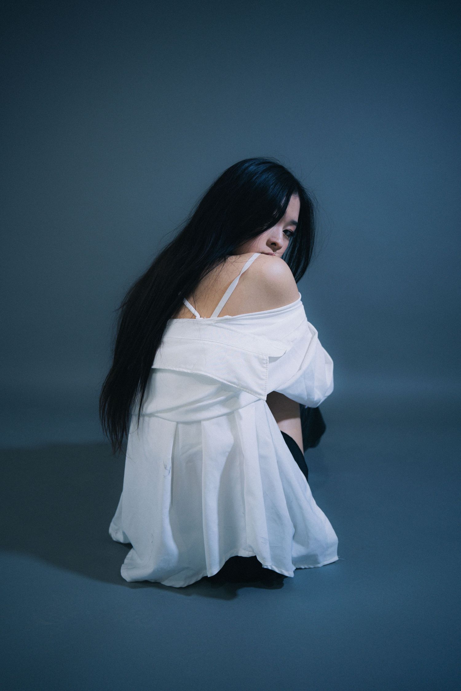 Artistic moody portrait in white dress against dark background shows contrasting shadows and flowing long hair.