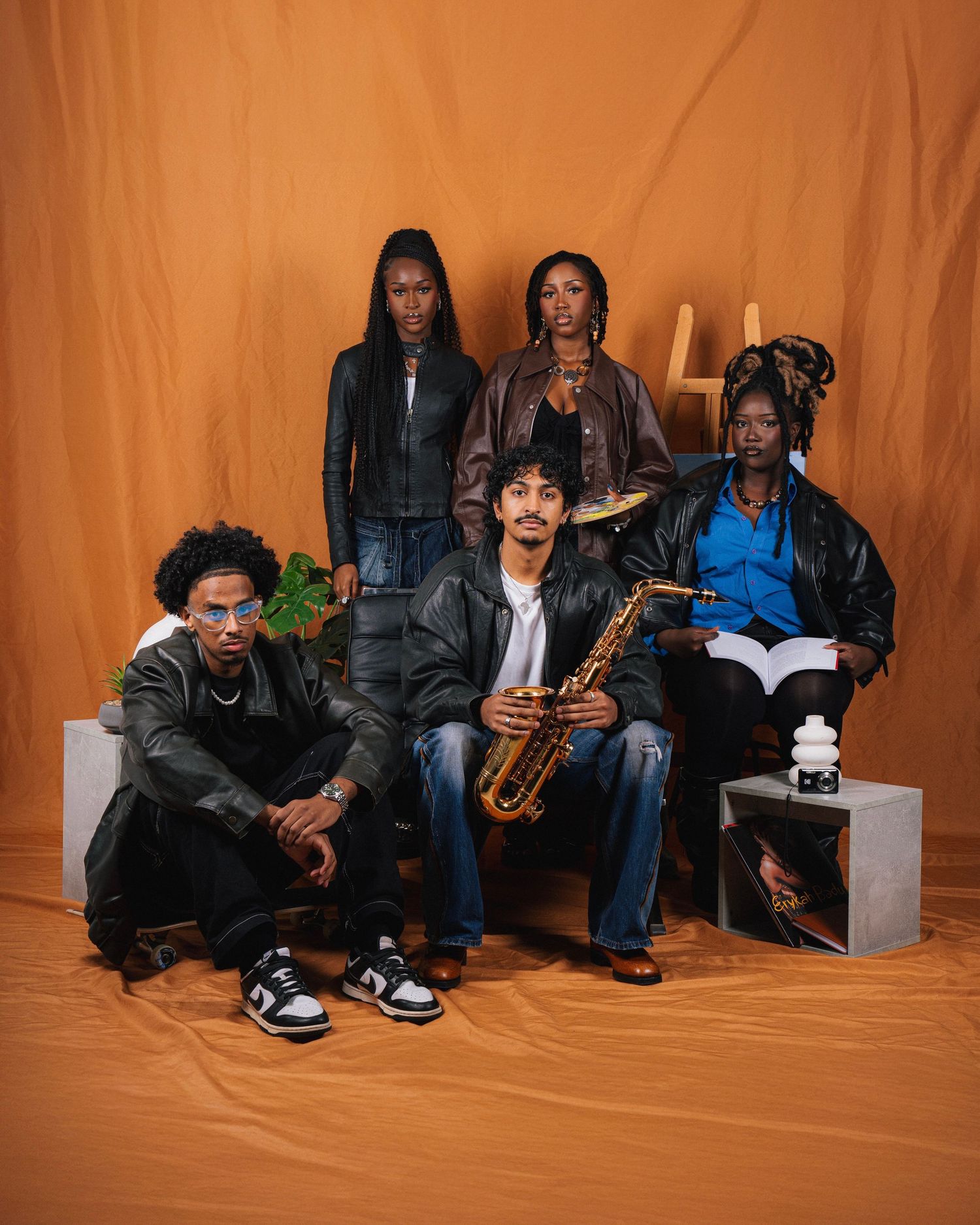 A group of musicians pose with instruments against an orange backdrop in an artistic studio portrait.