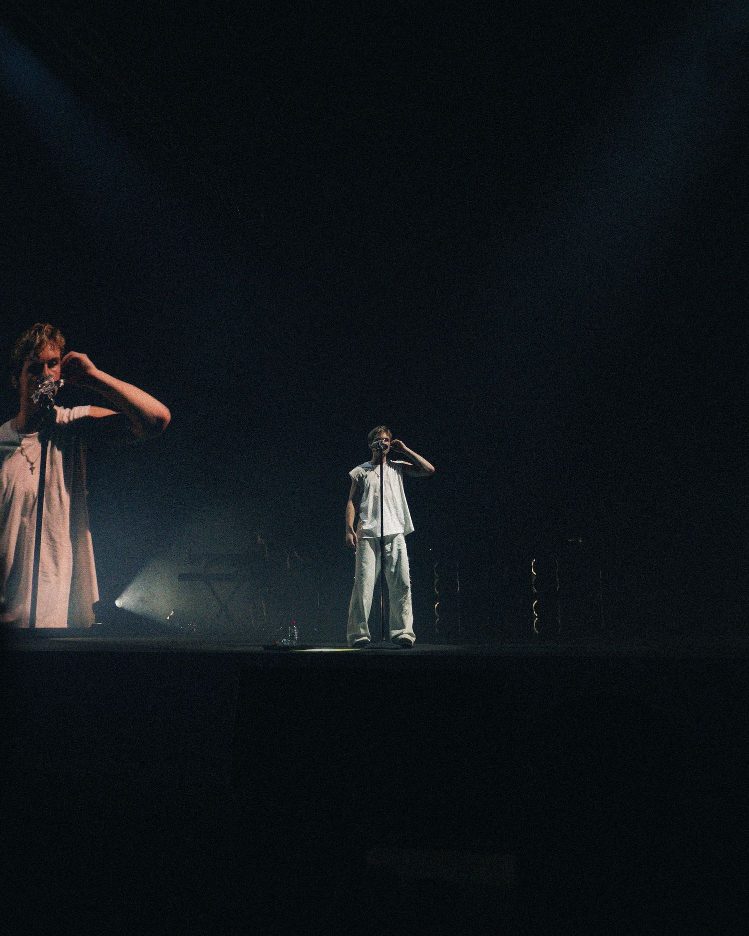 Two performers in silhouette on a dark stage, one wearing a dress and one in white, both gesturing dramatically.