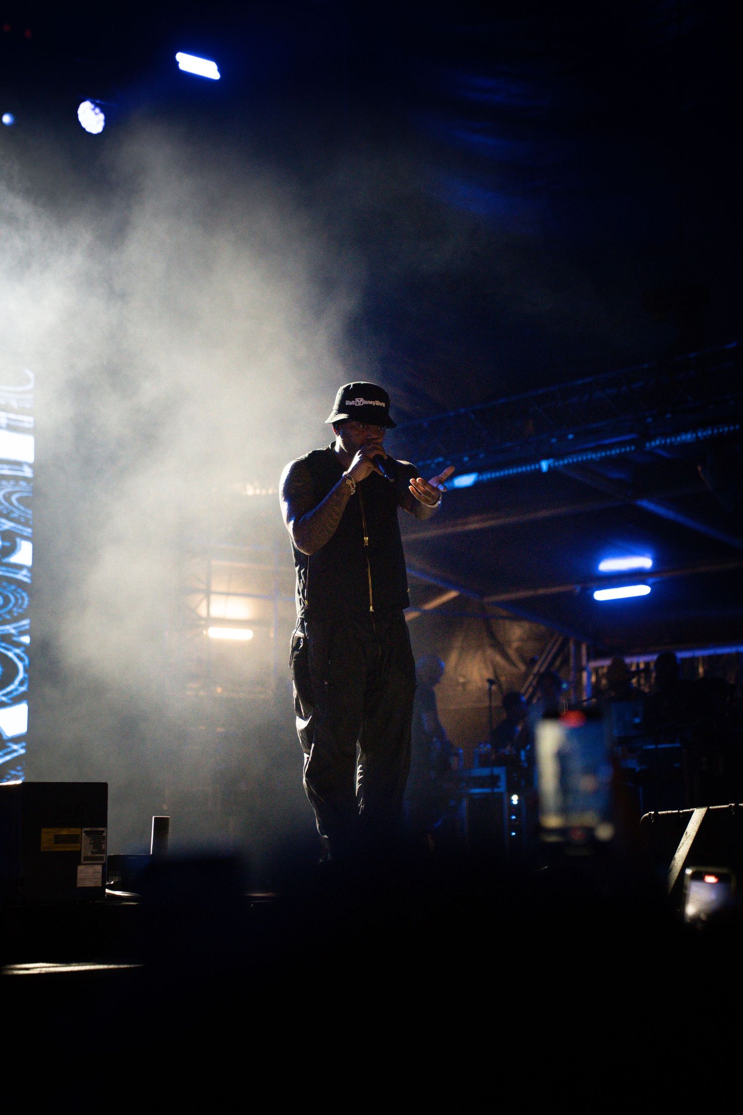 Silhouetted performer stands on stage in smoky atmosphere with dramatic blue lighting during concert performance.