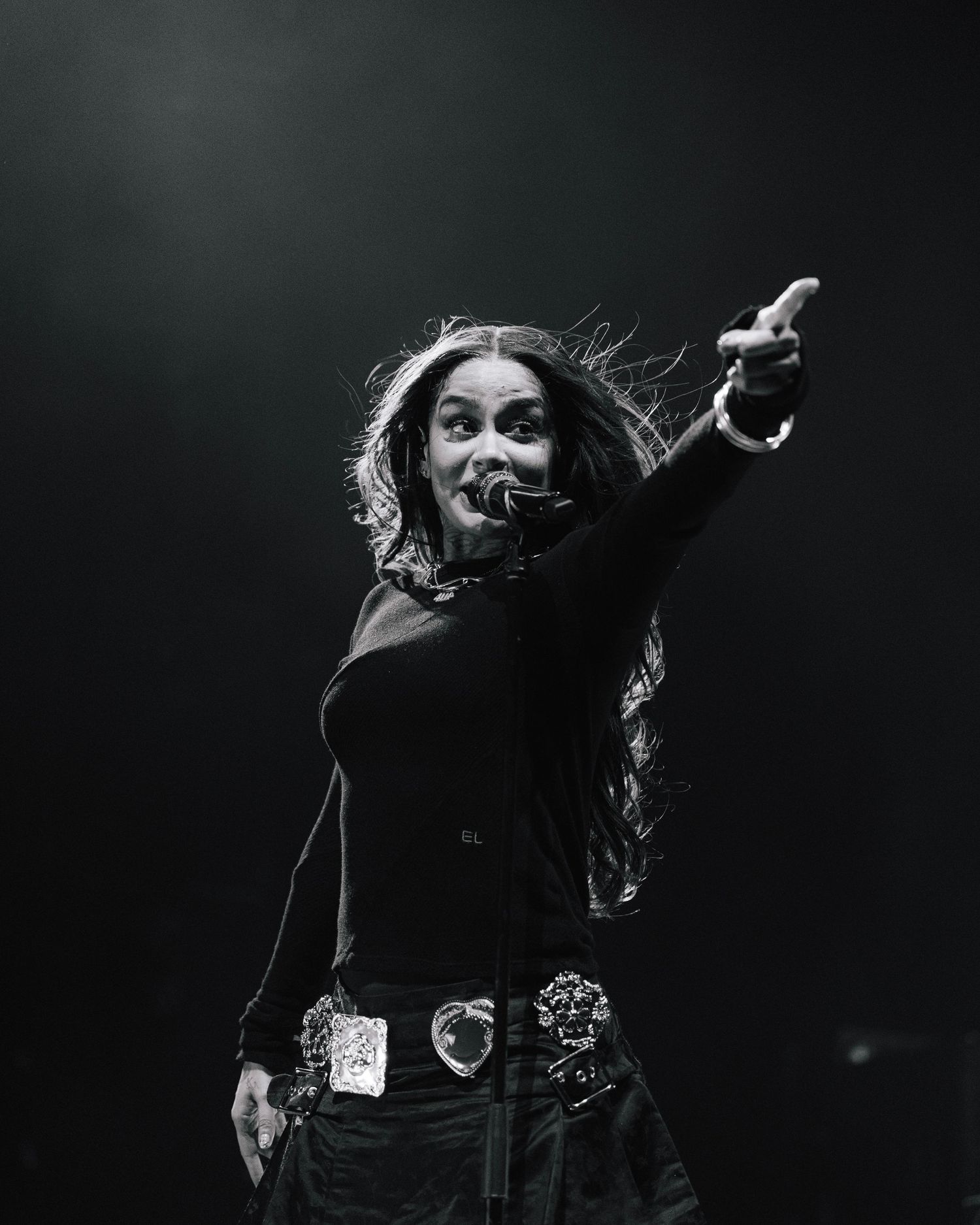 Dynamic black and white concert photo showing a performer in black clothing with flowing hair pointing outward.