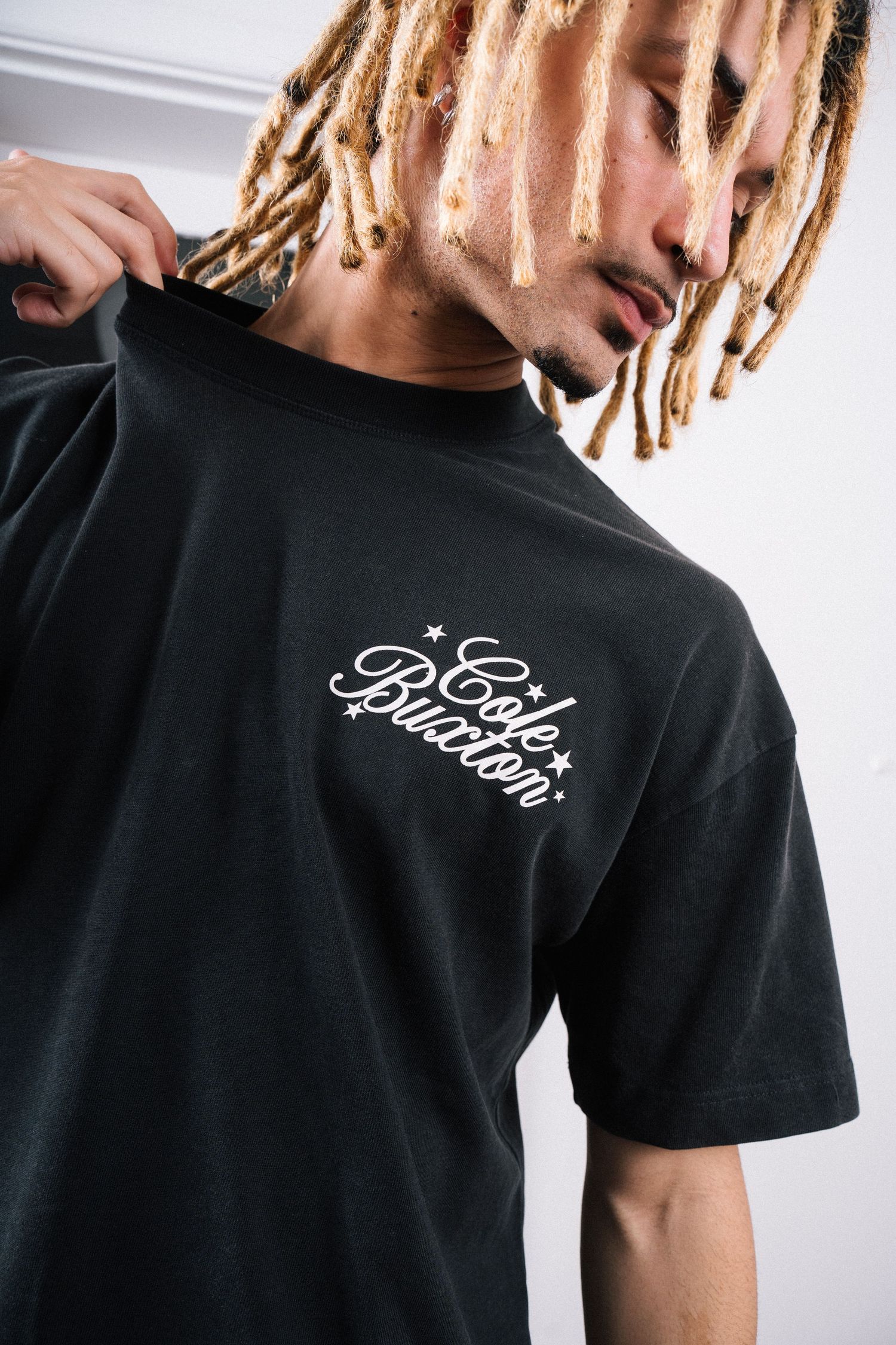 Person wearing a black t-shirt with blonde dreadlocks and script logo design on the chest.