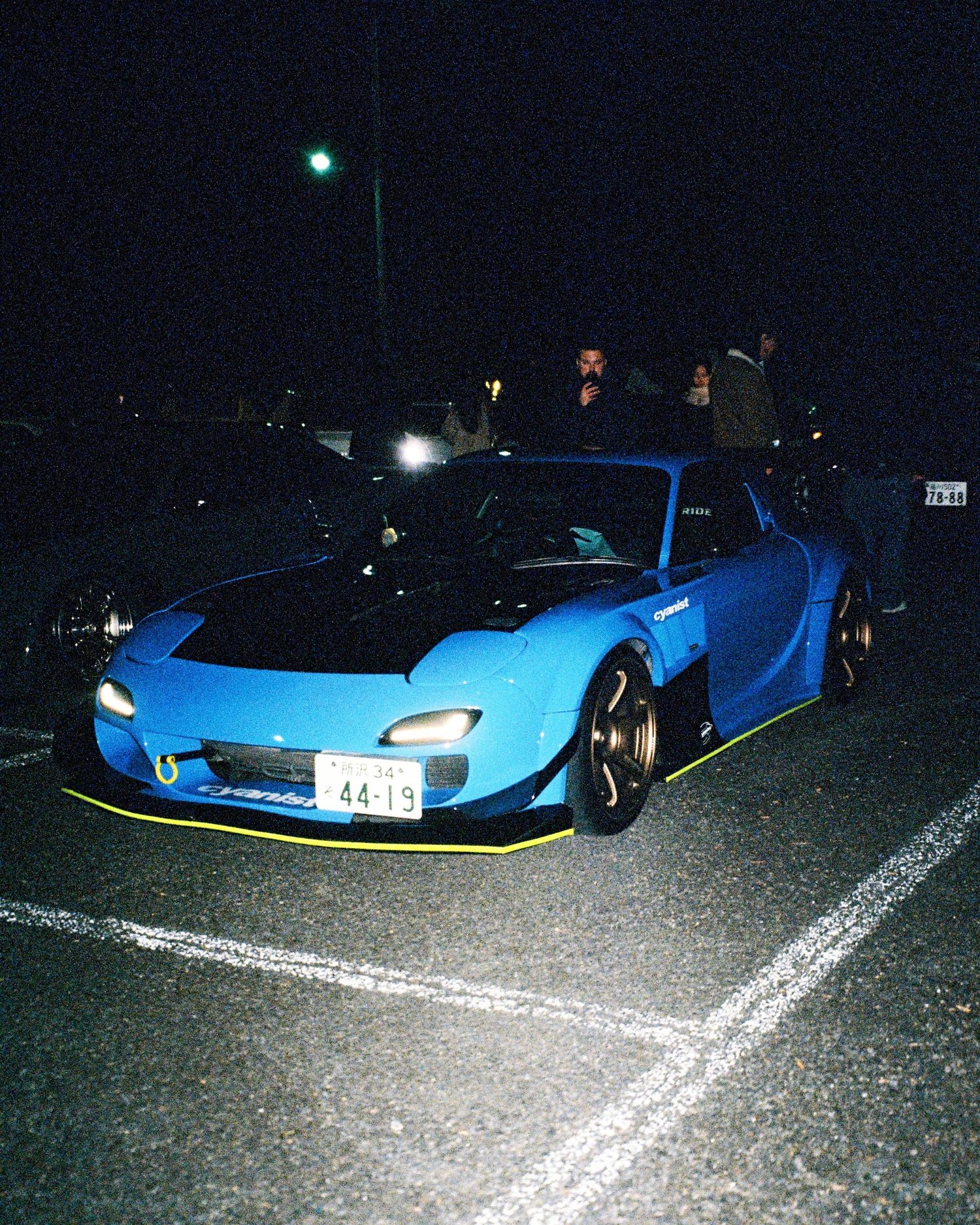 Light blue modified Mazda RX-7 with wide body kit parked at night.