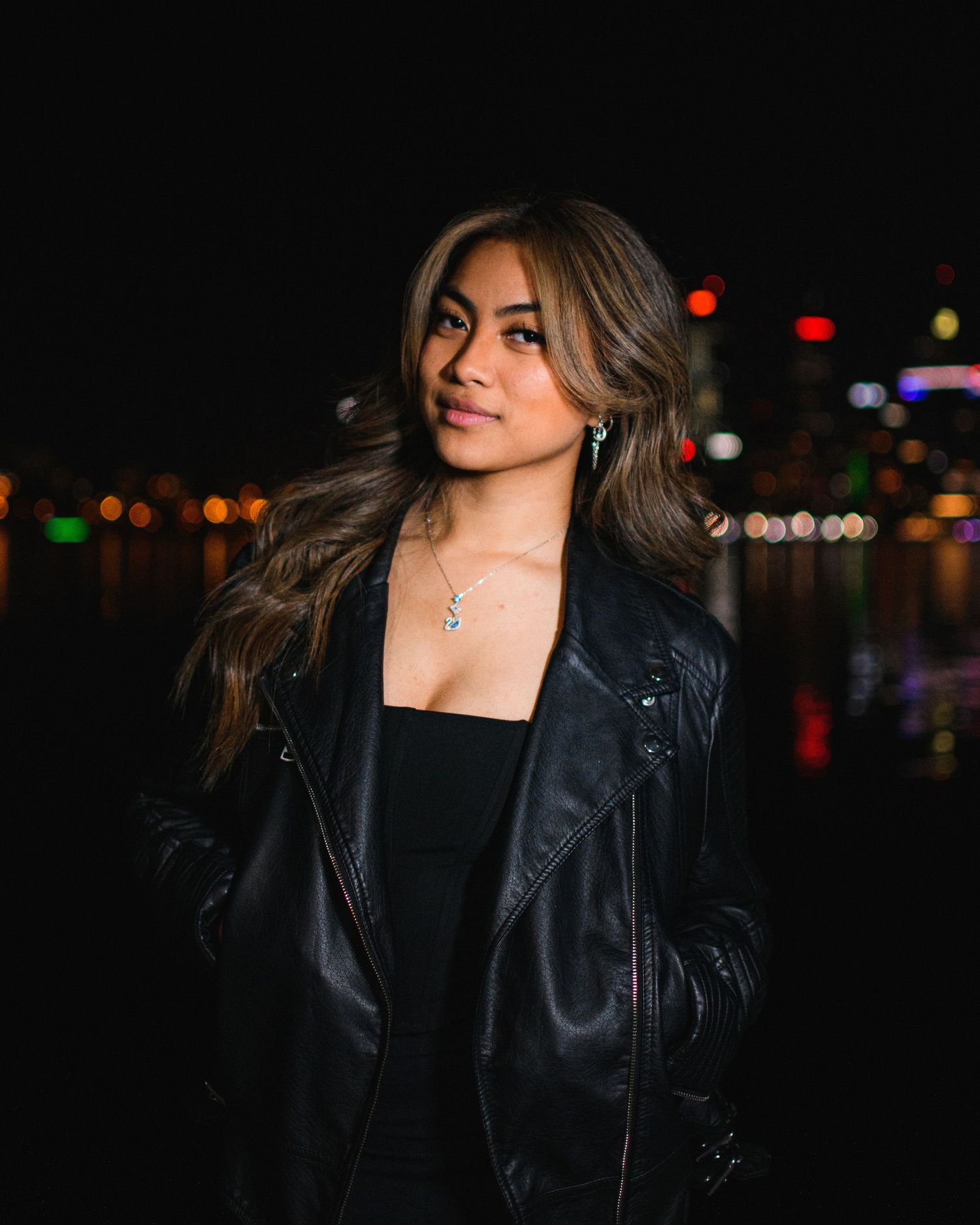 Nighttime portrait of woman in leather jacket with city lights in background.