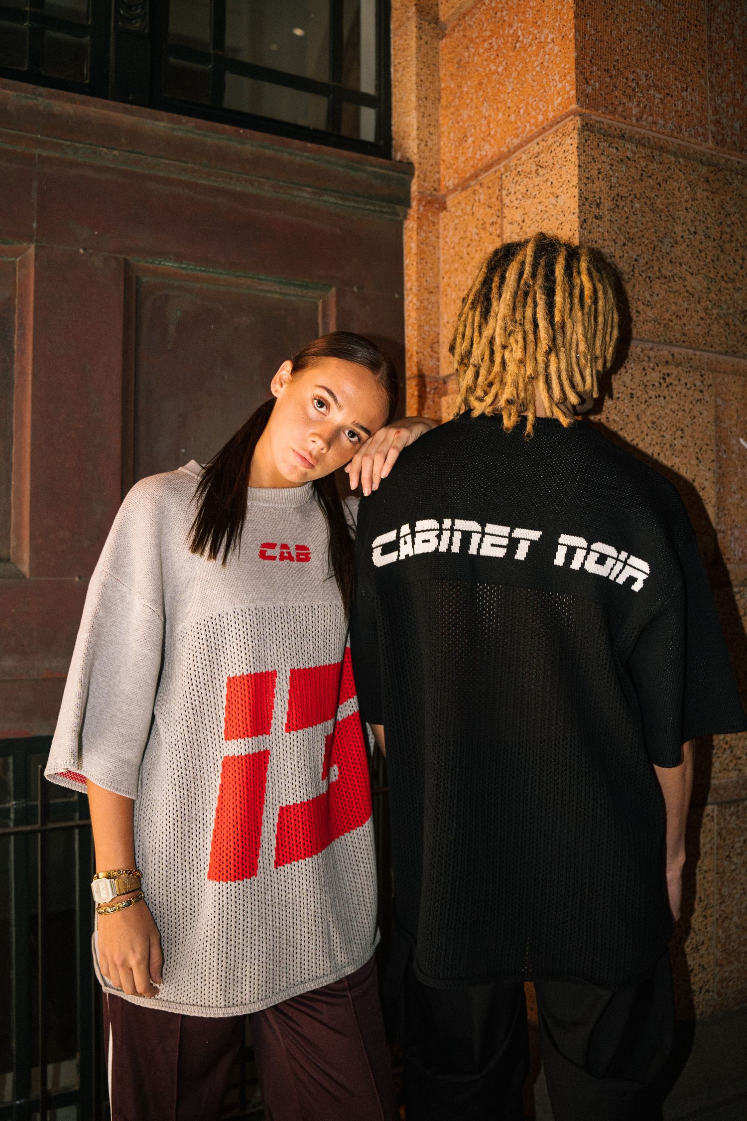 Two people model streetwear with one wearing Cabinet Noir text on back.