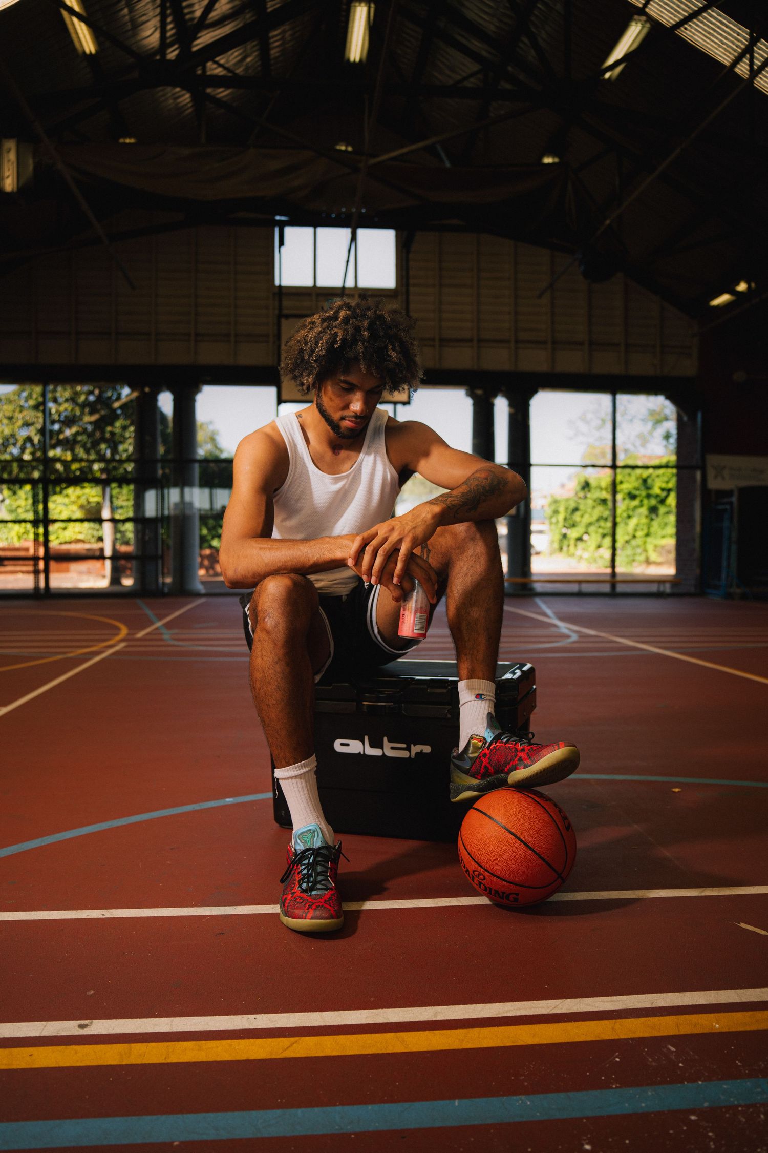 Basketball player taking a break while sitting on equipment in an indoor court.