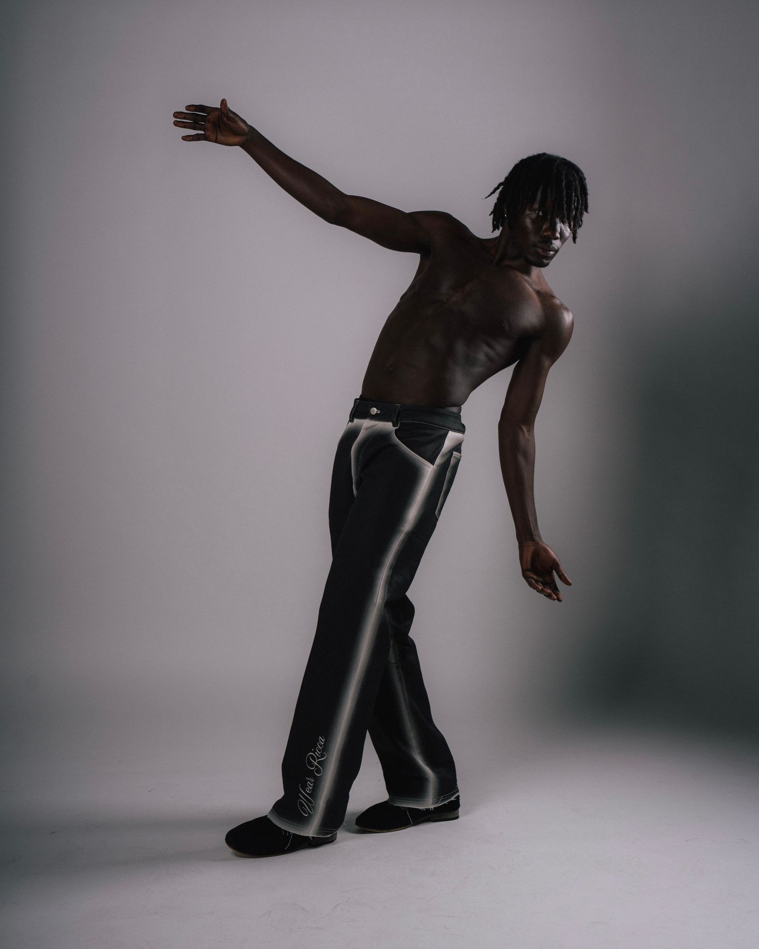 Artistic dance pose silhouette with person in black pants against light background.