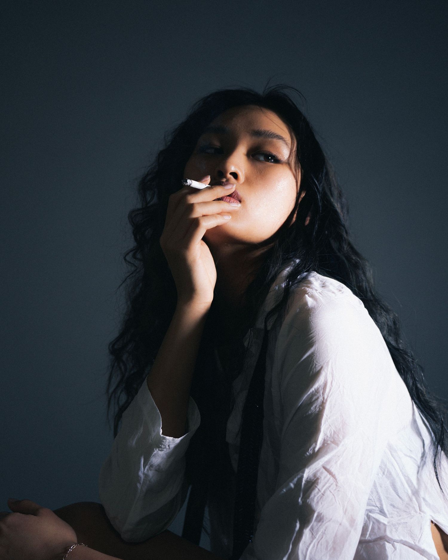 Moody portrait of a figure in white clothing against dark background with dramatic lighting.