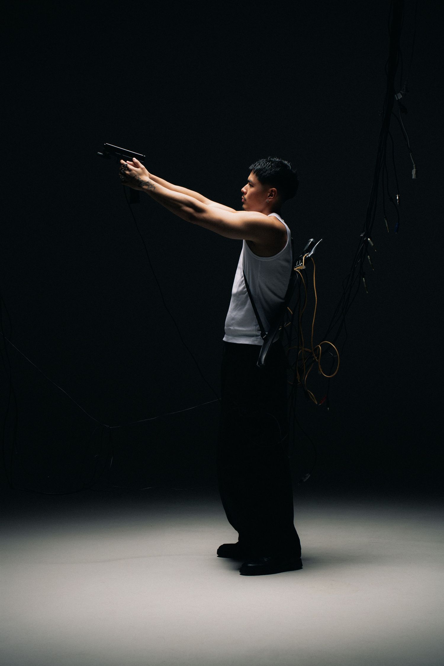 Athletic dancer in a gray tank top and dark pants strikes a dramatic pose against a dark backdrop in a studio.