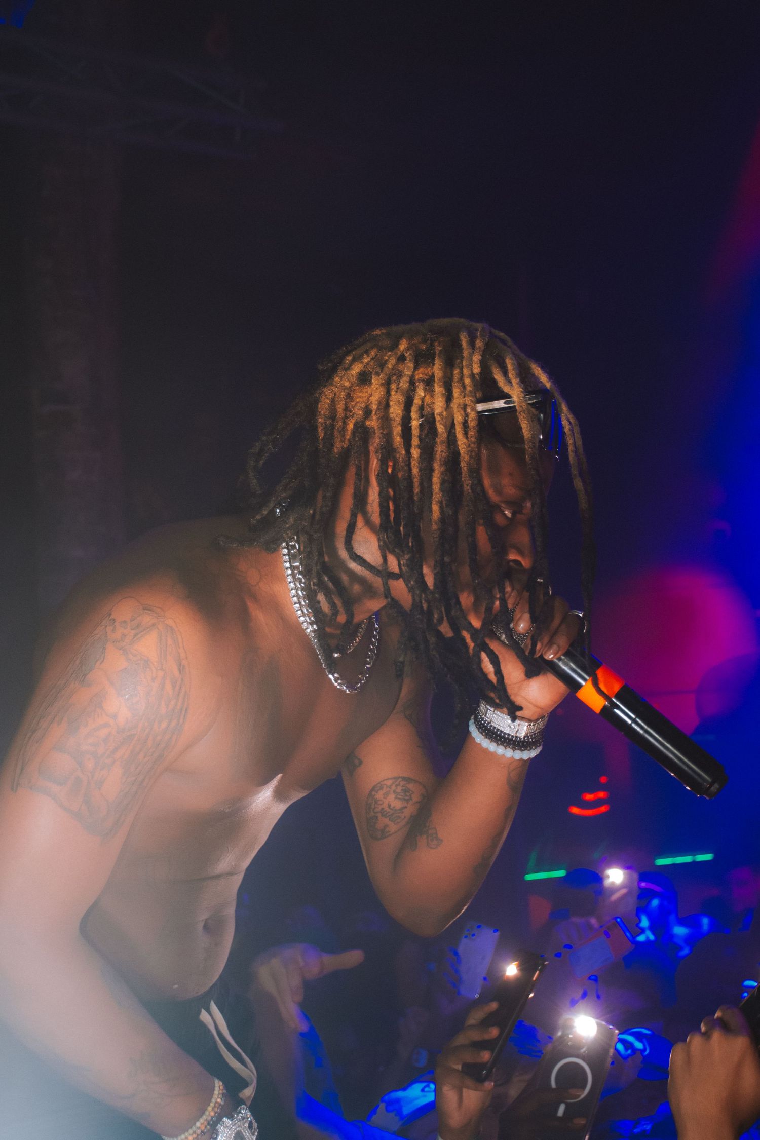 Shirtless performer with dreadlocks and chains singing during nightclub performance.