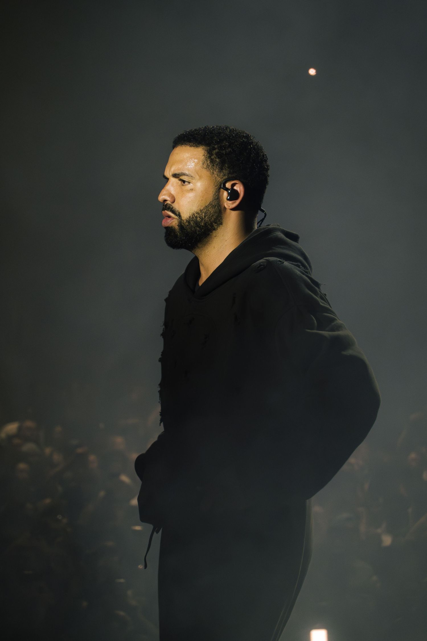 Performer in a black hoodie illuminated on stage with dramatic lighting and haze effects.