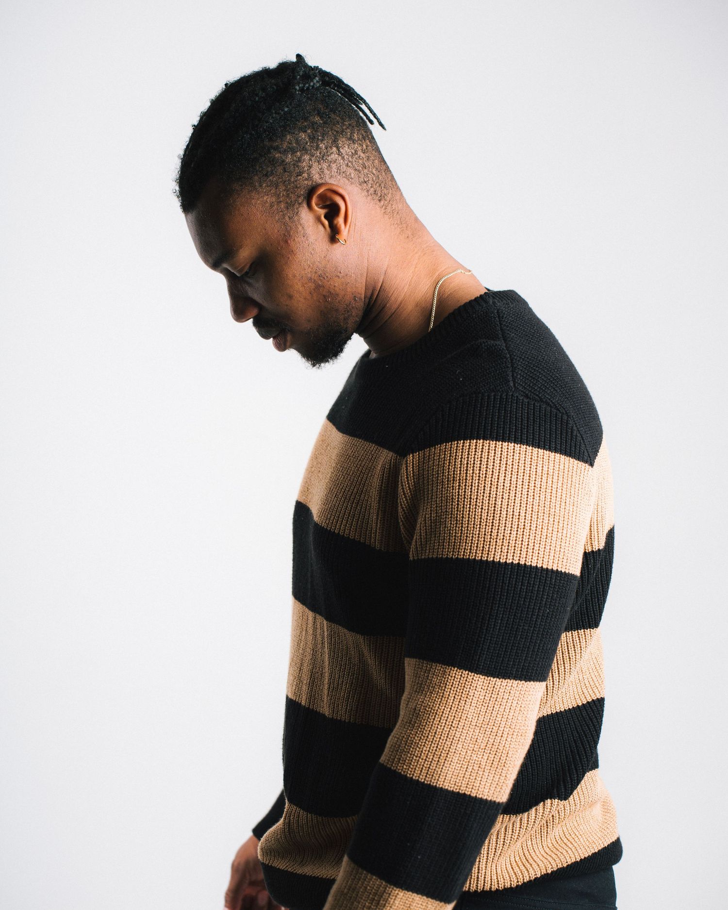 Side profile view of someone wearing a black and tan striped ribbed sweater against a white background.