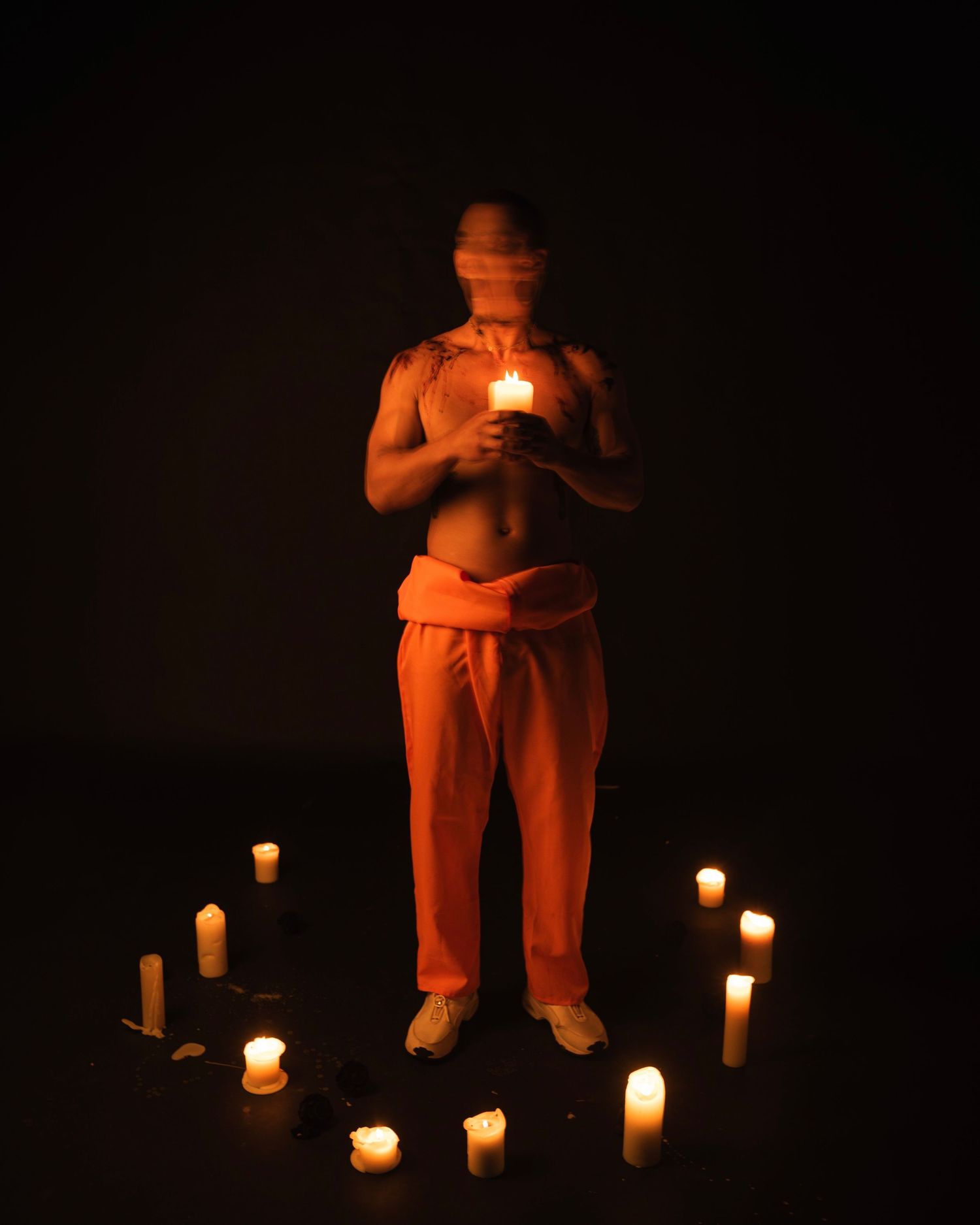 A dimly lit scene with a figure sitting in a chair surrounded by glowing candles casting warm orange light in darkness.