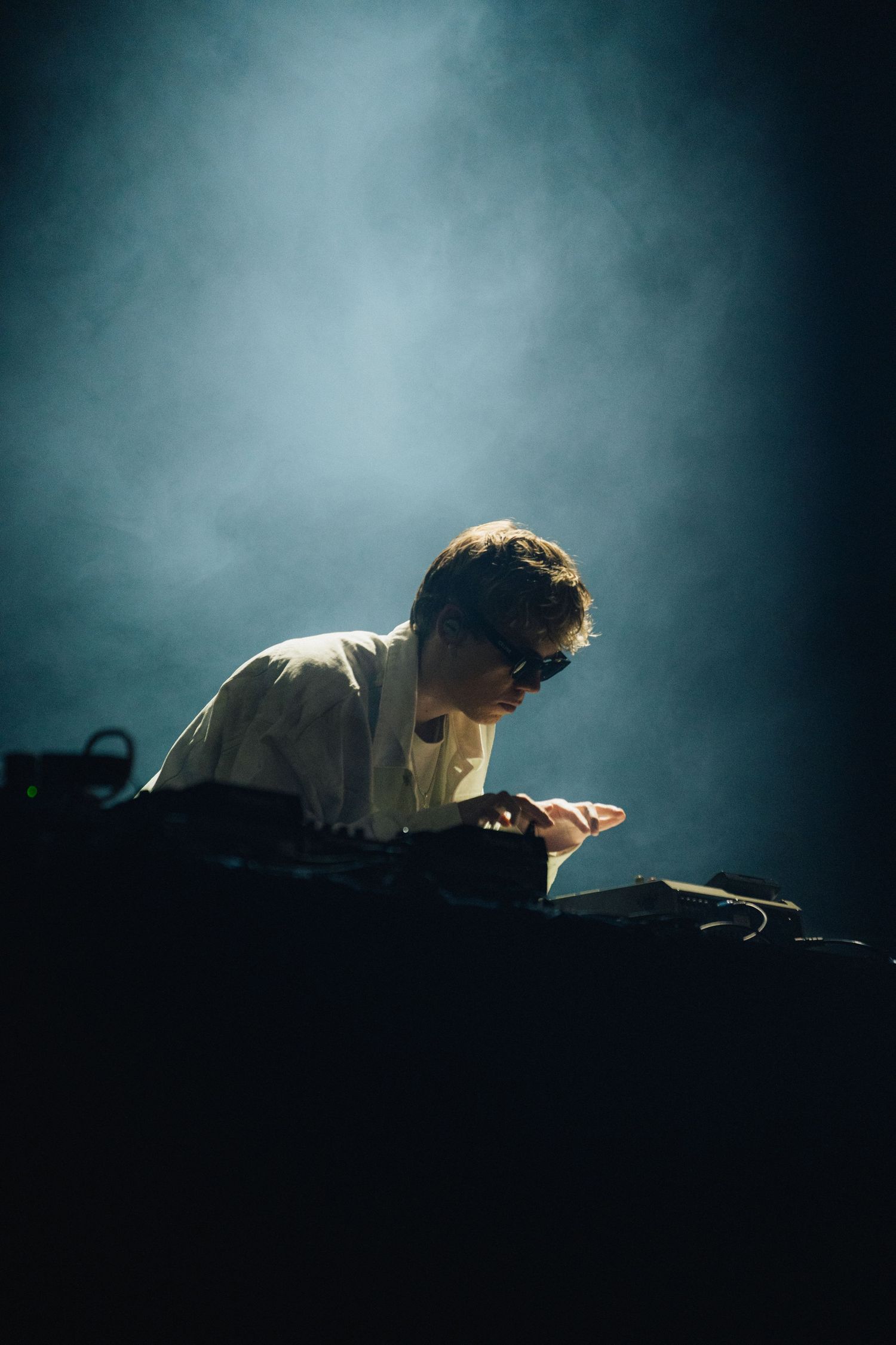 Musician performs at a dark concert venue with dramatic backlighting creating a moody silhouette effect against smoky atmosphere.