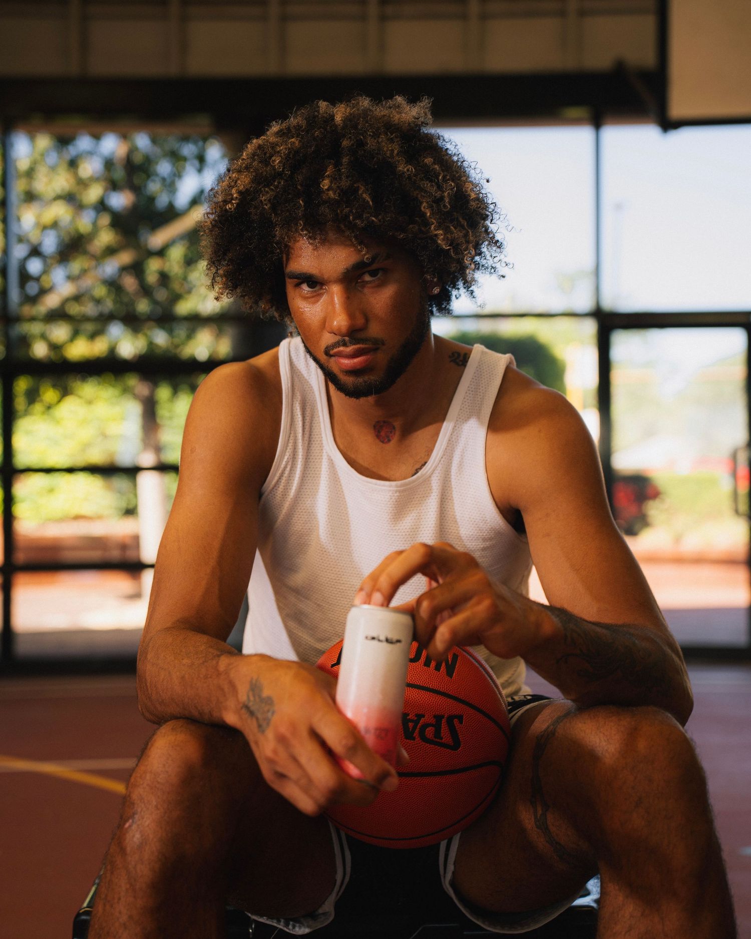 Basketball player in white tank top holding ball and drink on indoor court.
