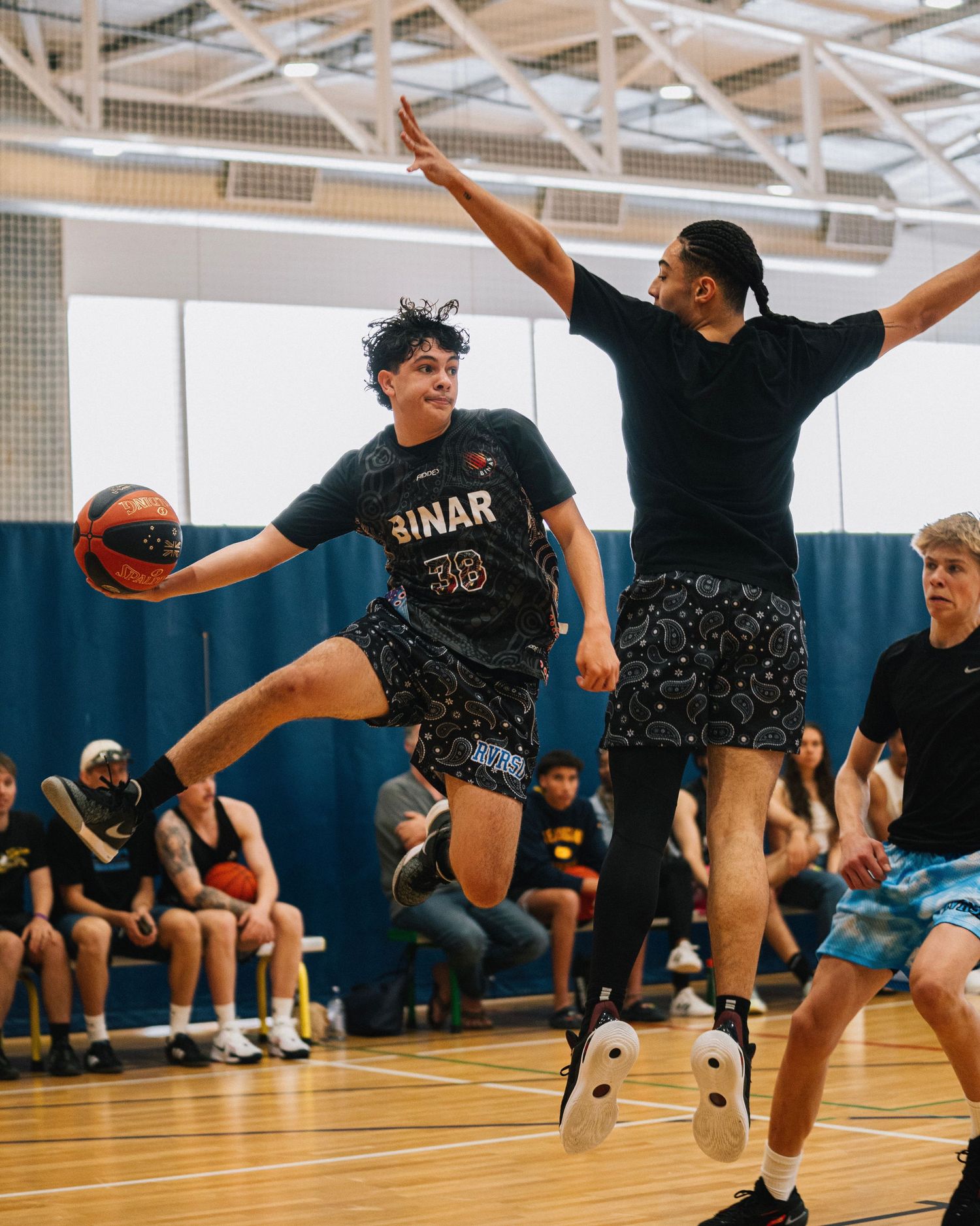 Players in a competitive basketball game making athletic moves on the indoor court.