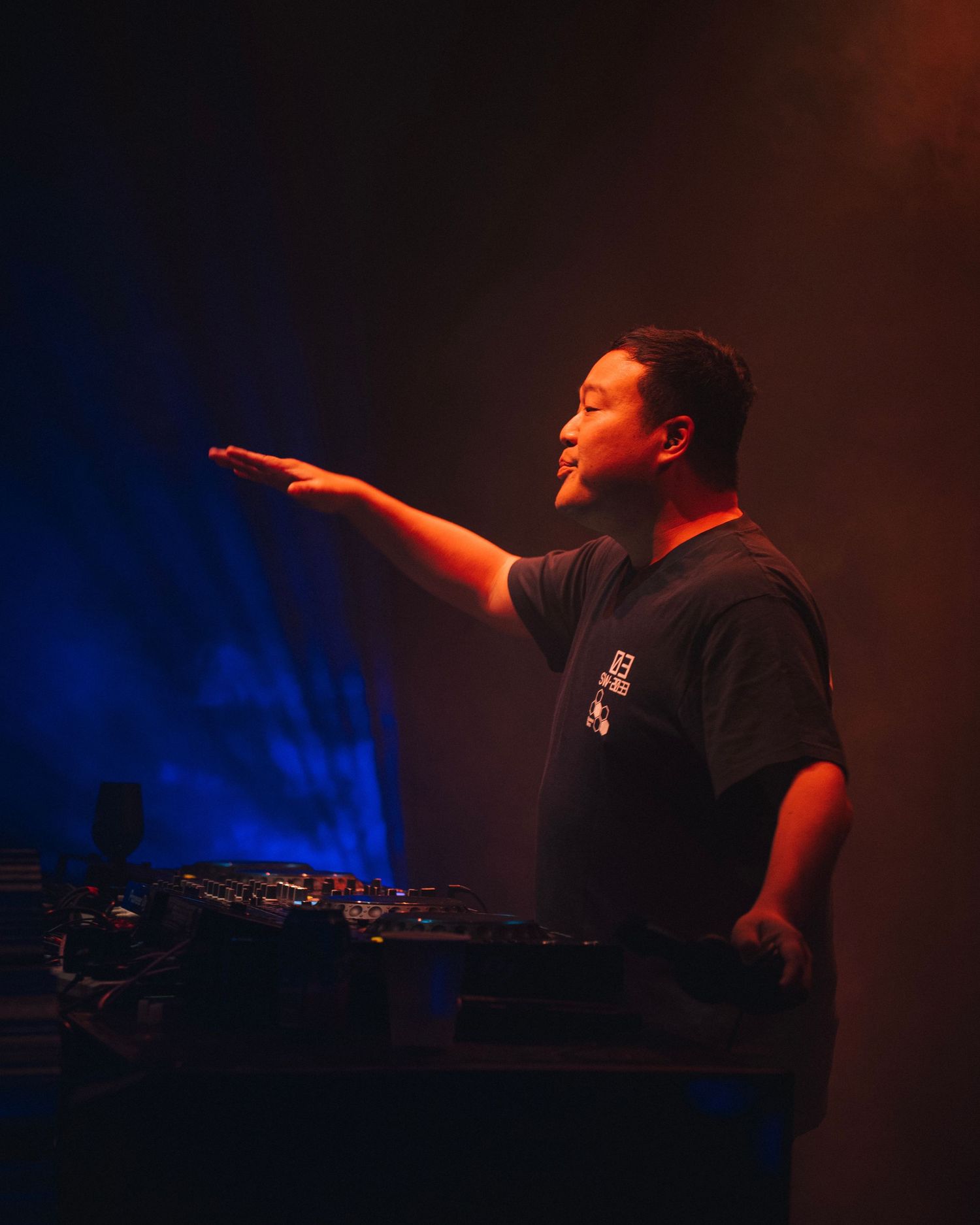 DJ gestures to crowd while performing on dark stage with blue lighting.
