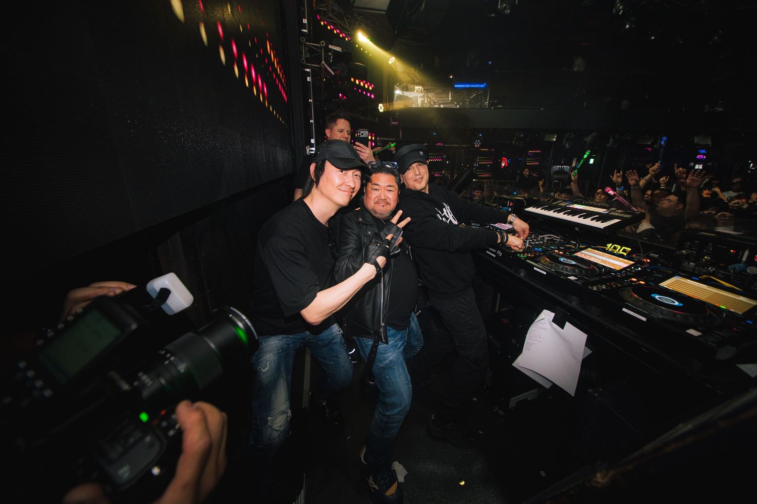 DJ performs at a dark nightclub with colorful lights illuminating the equipment and dance floor.