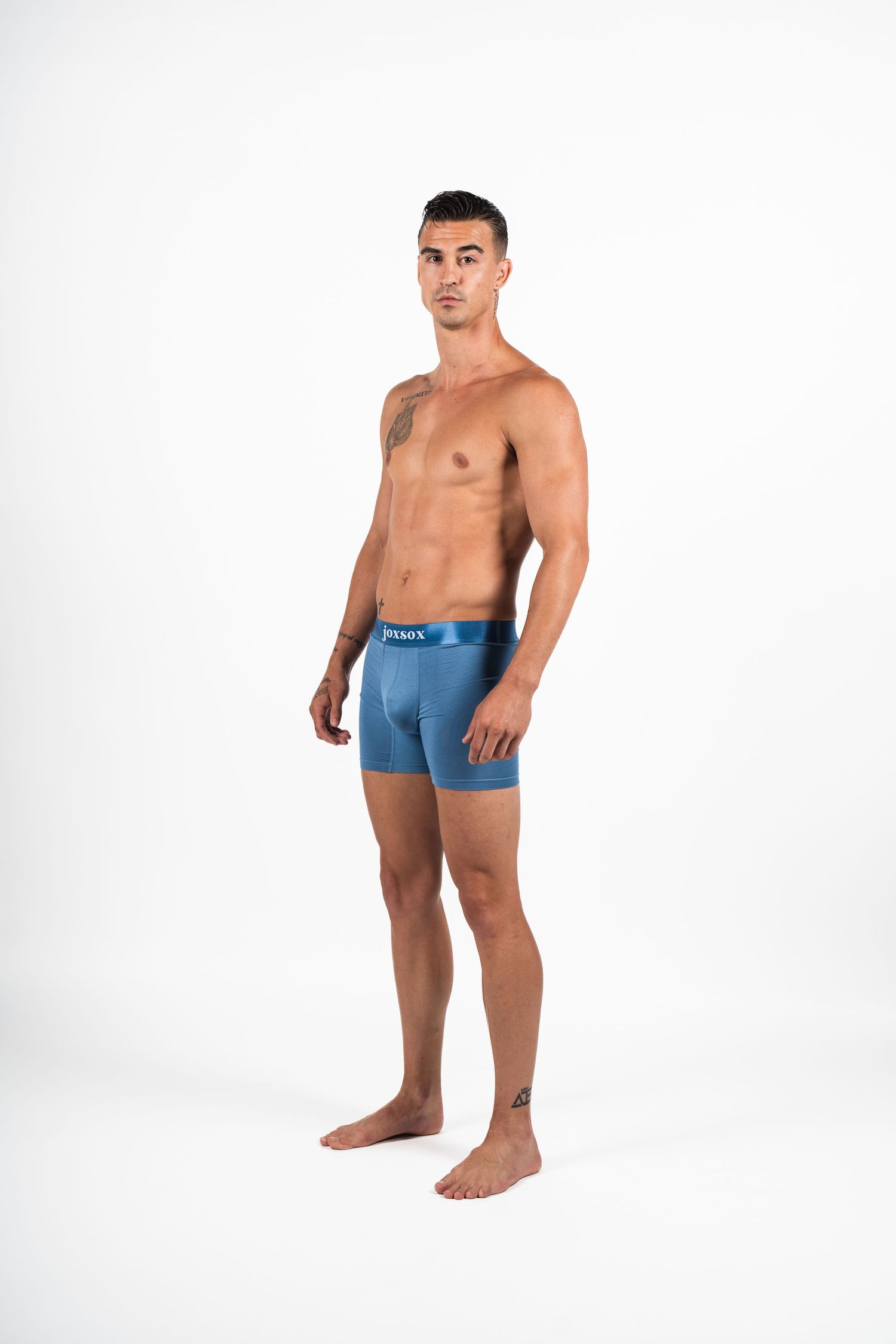 Athletic model wearing blue boxer briefs poses against white background showing muscular physique.