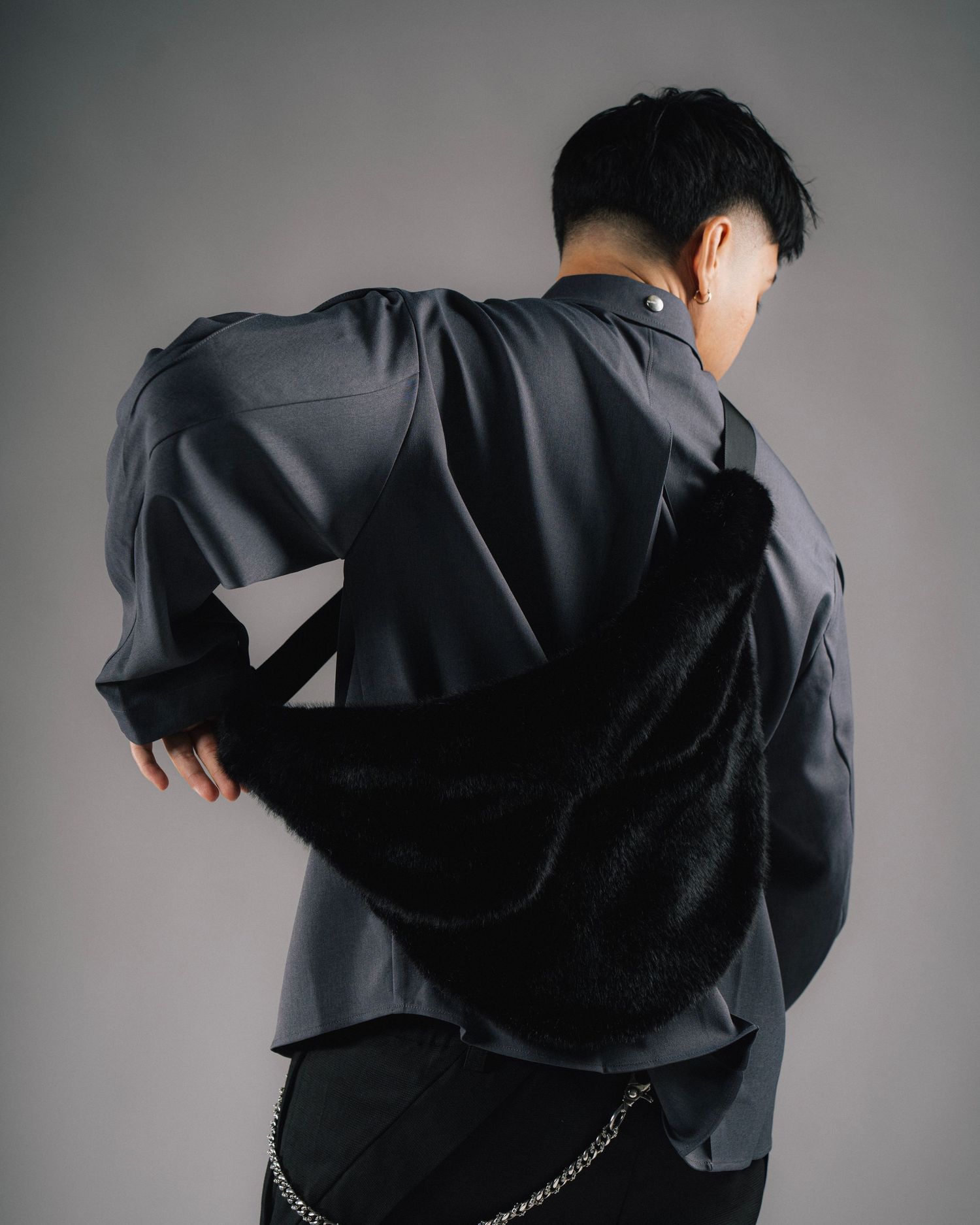 Back view of person wearing dark jacket with geometric design against gray background.