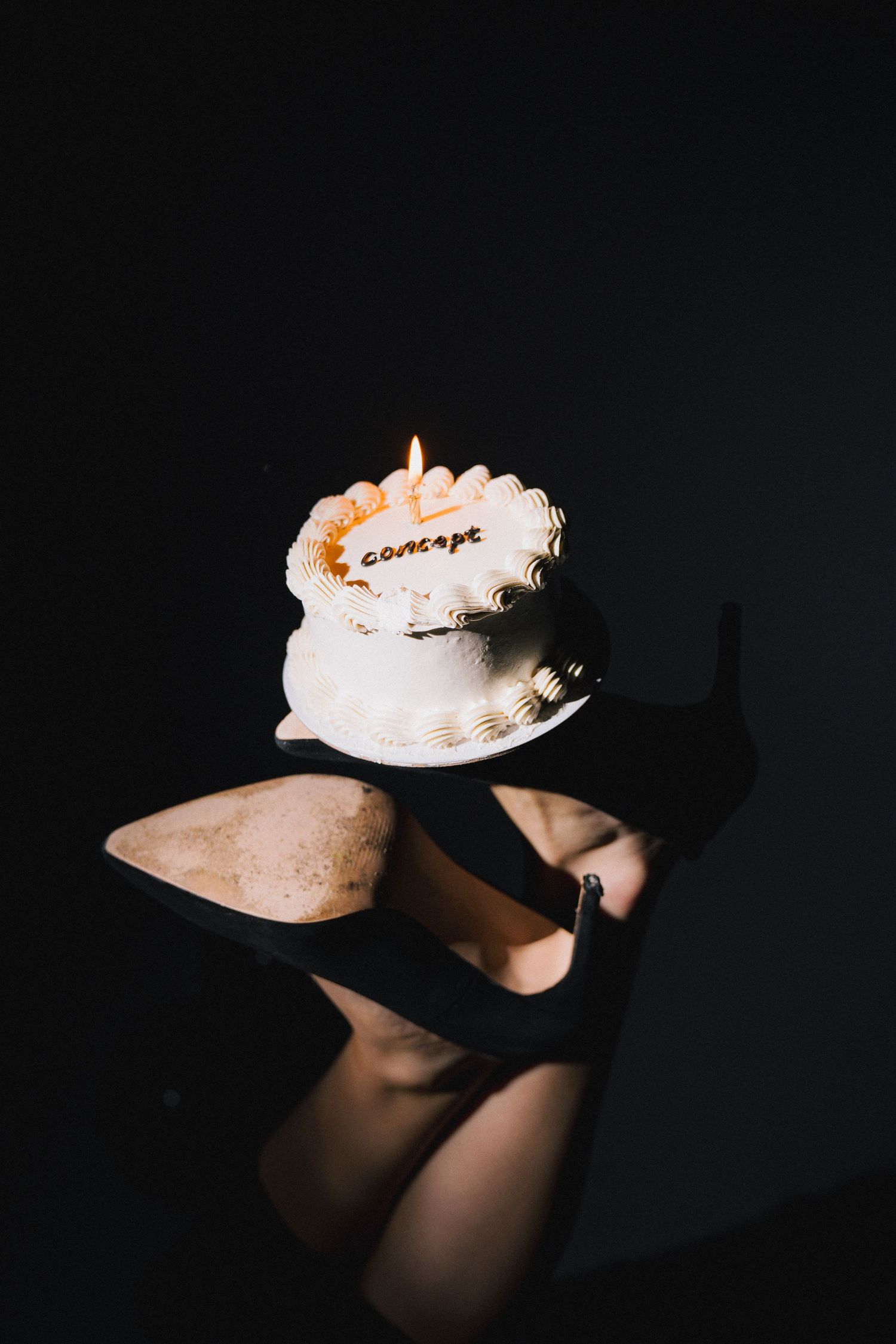 Artistic photo of a cake with candle and high heels in dark moody lighting.