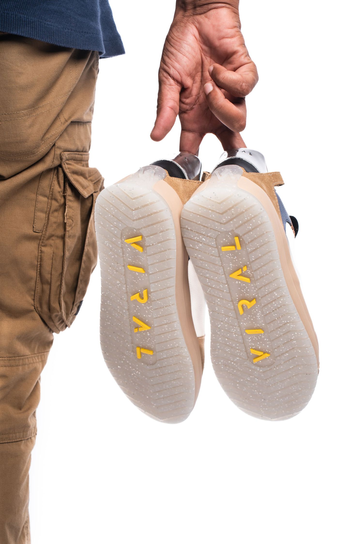 Close-up of hand holding pair of sneakers showing yellow text on soles against white background.