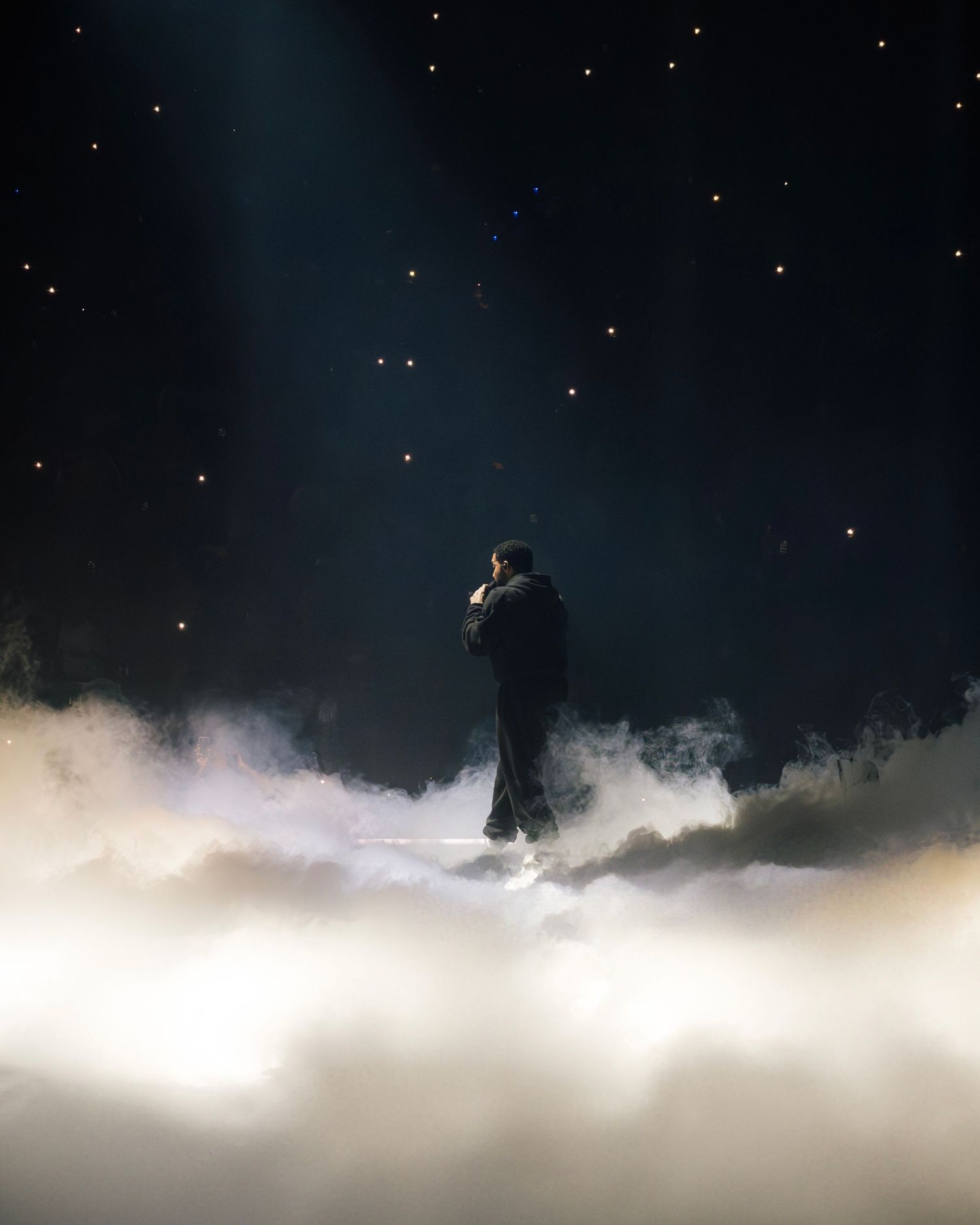 A silhouette stands amid dreamy clouds under a starlit night sky creating a surreal atmospheric scene.