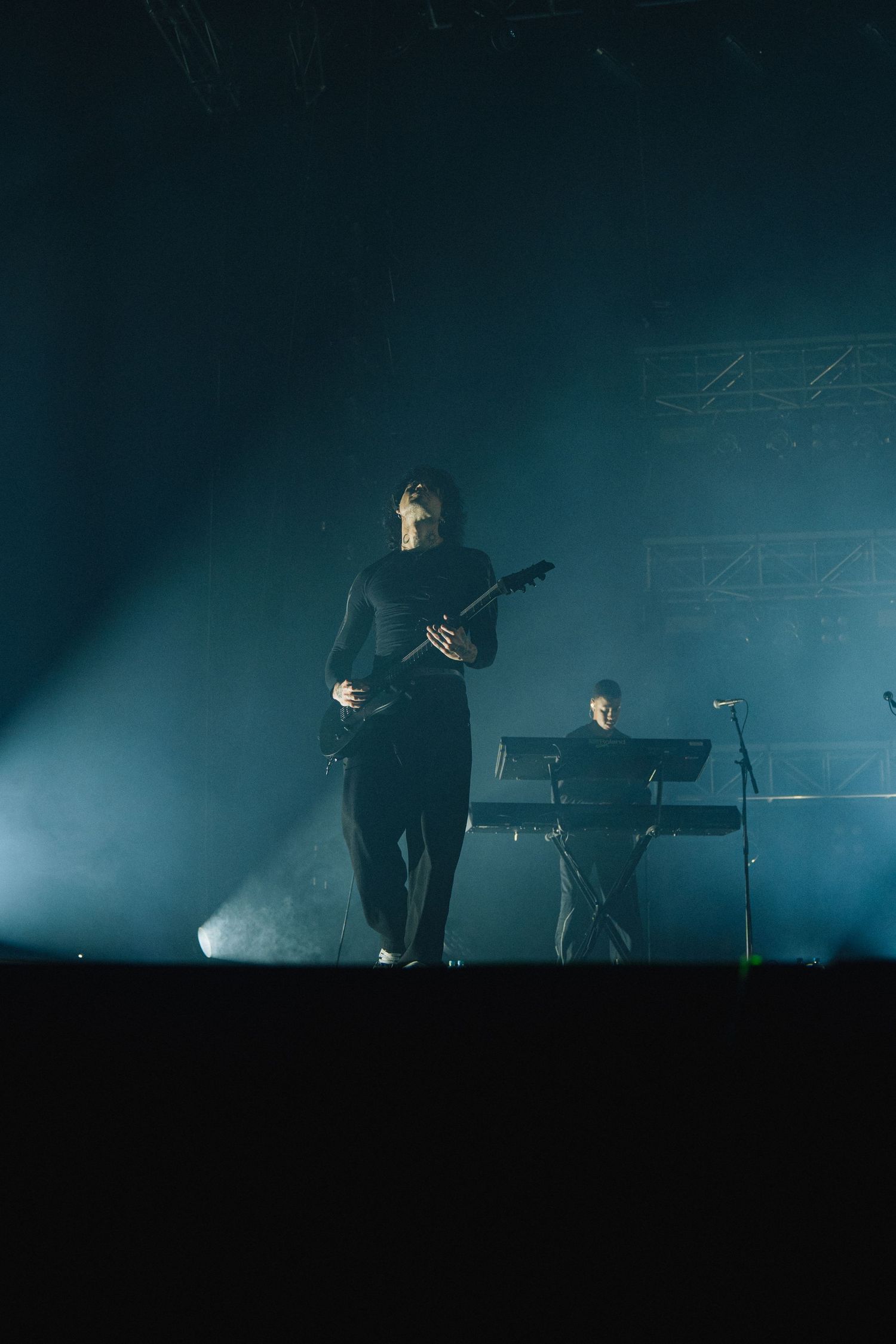 Musicians perform on a smoky stage with dramatic blue lighting during a concert performance.