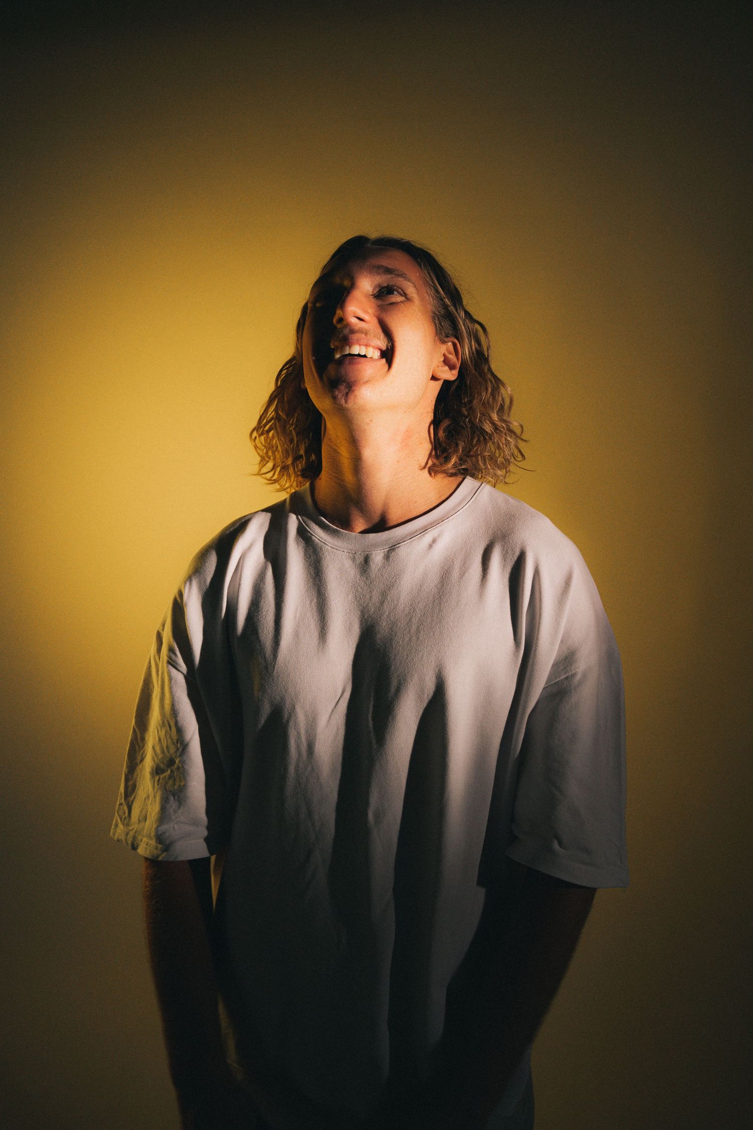 Someone wearing a light colored t-shirt laughs joyfully against a warm yellow background.