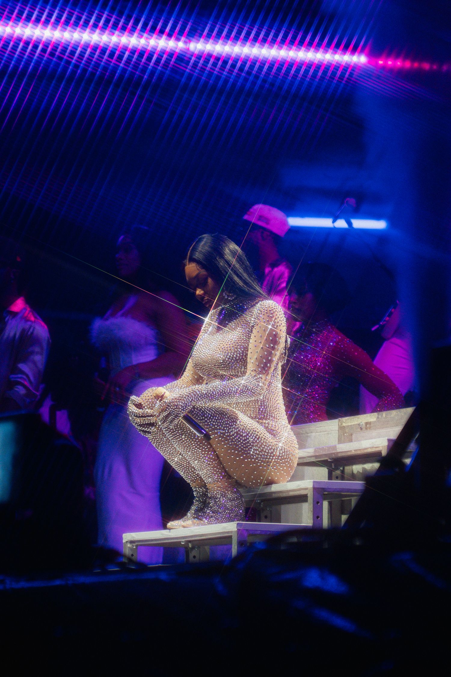 Illuminated crystal-like sculpture sits on white platform under purple and blue nightclub lighting.