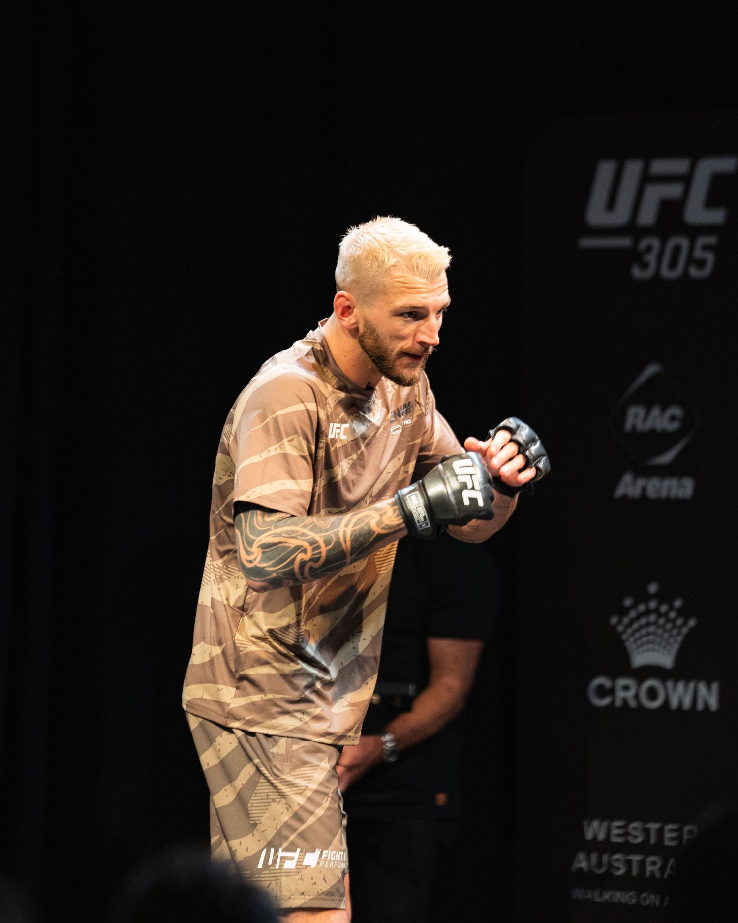 Fighter in tan outfit celebrates during UFC 305 event at Crown Arena.